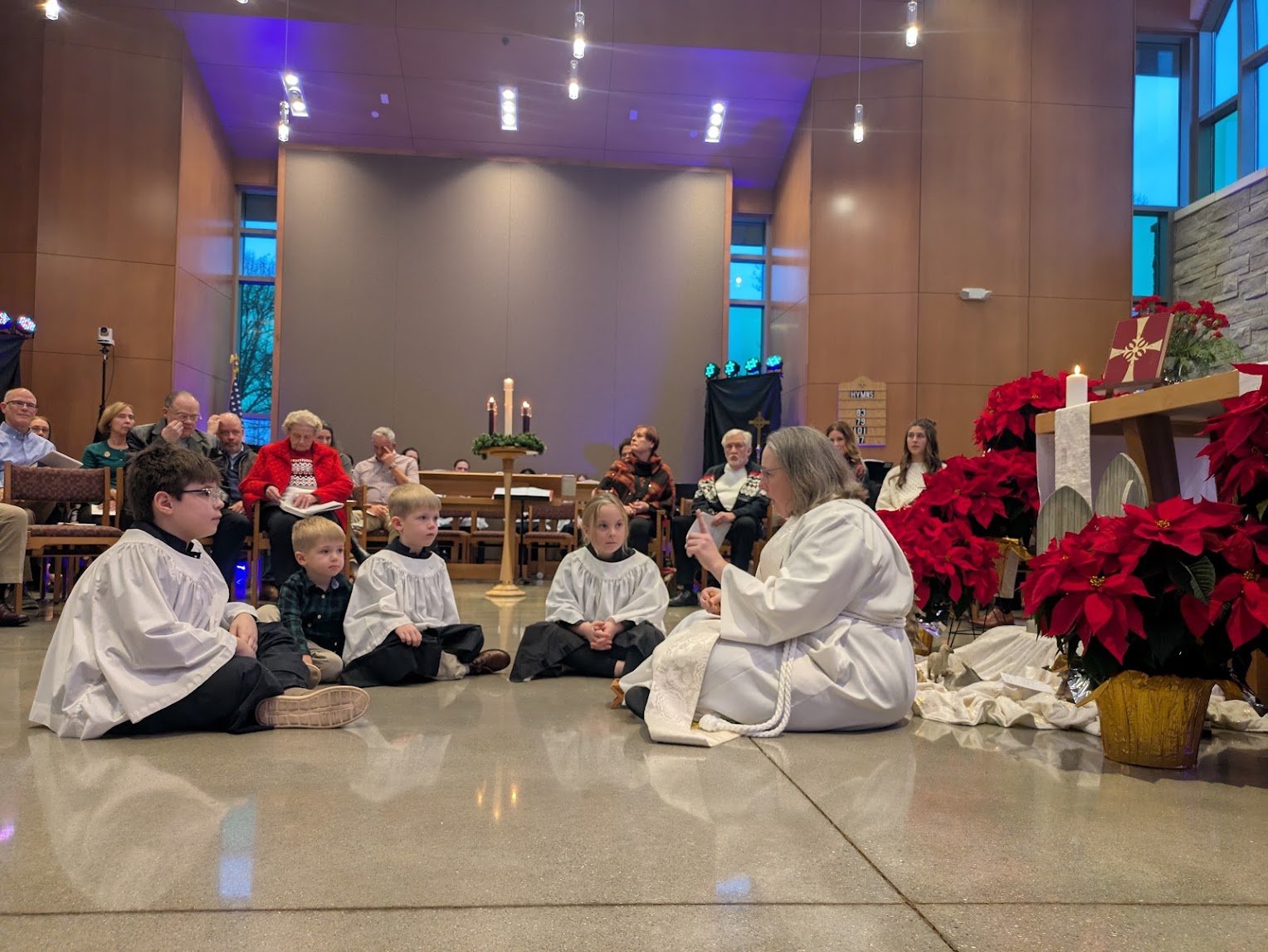 The Rev. Cameron O'Riley sitting on the floor with young children during a festive worship service at Christ Church Glendale in Glendale, Ohio.