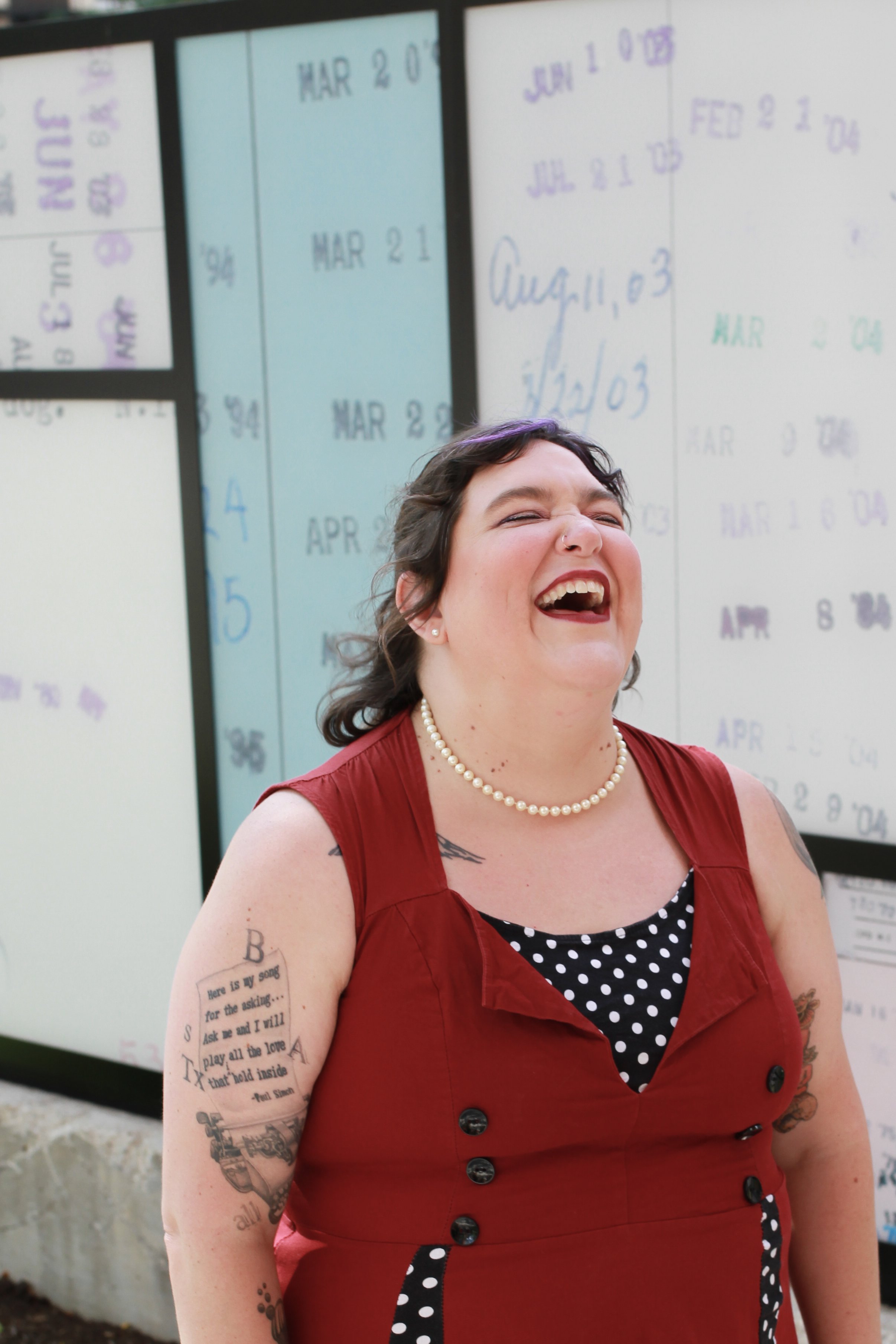 The found of Mycelium Creations laughing. She's wearing a red dress with black accents and a string of pearls