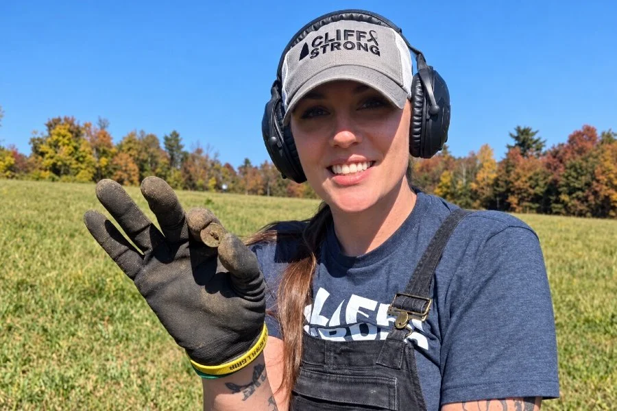 Bre the Metal BREtectorist from Quarter Hoarder posing with an old button she found metal detecting in a farm field