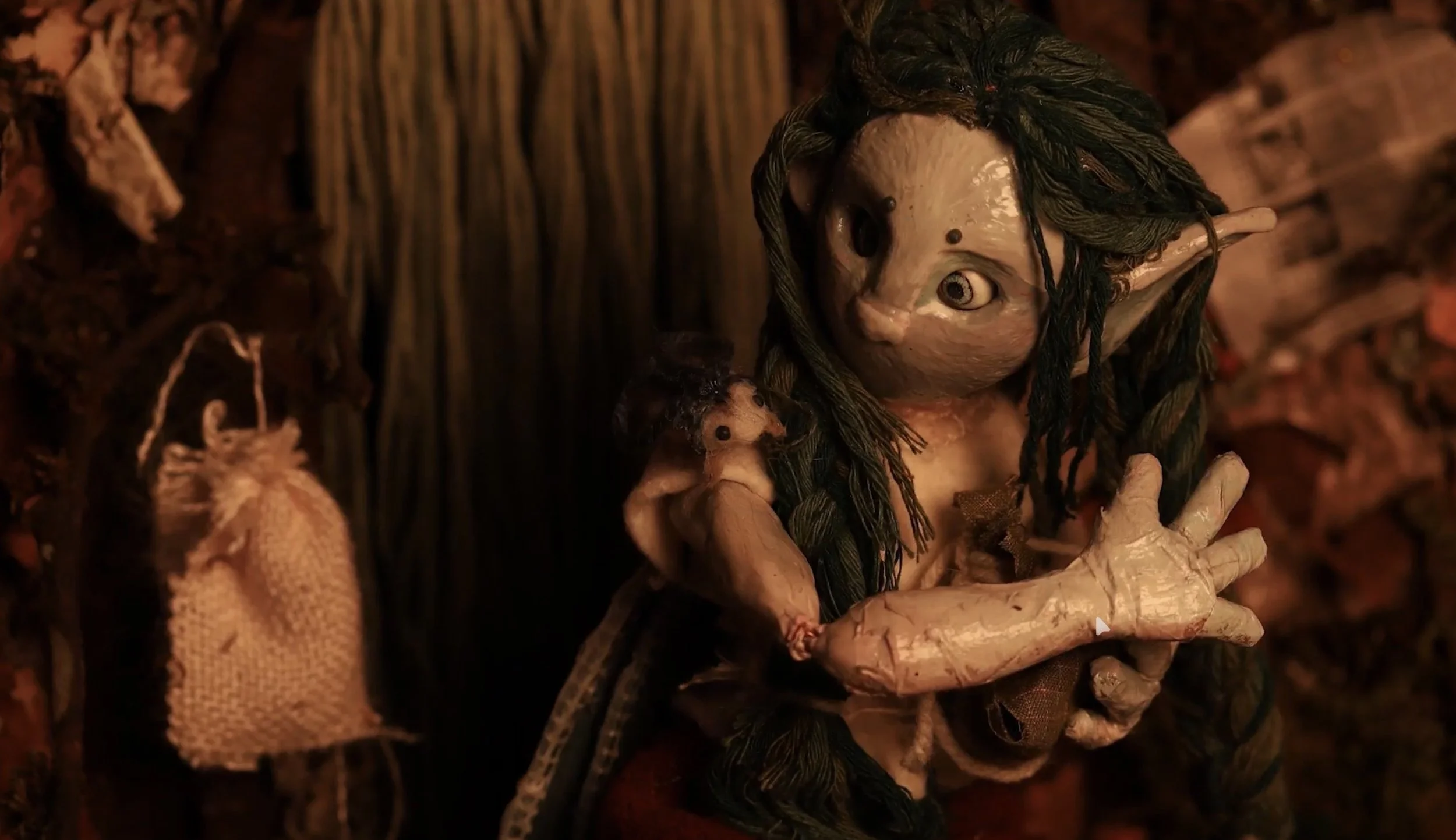A detailed puppet or sculpture of a fantasy creature with large eyes, pointy ears, and long dark hair, set against a dimly lit background.