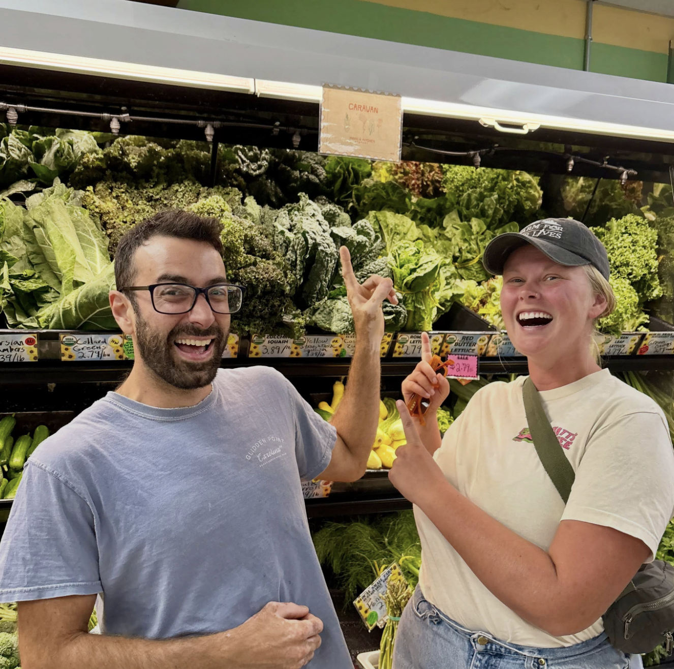 Two people smiling and pointing at leafy greens in a grocery store produce section.