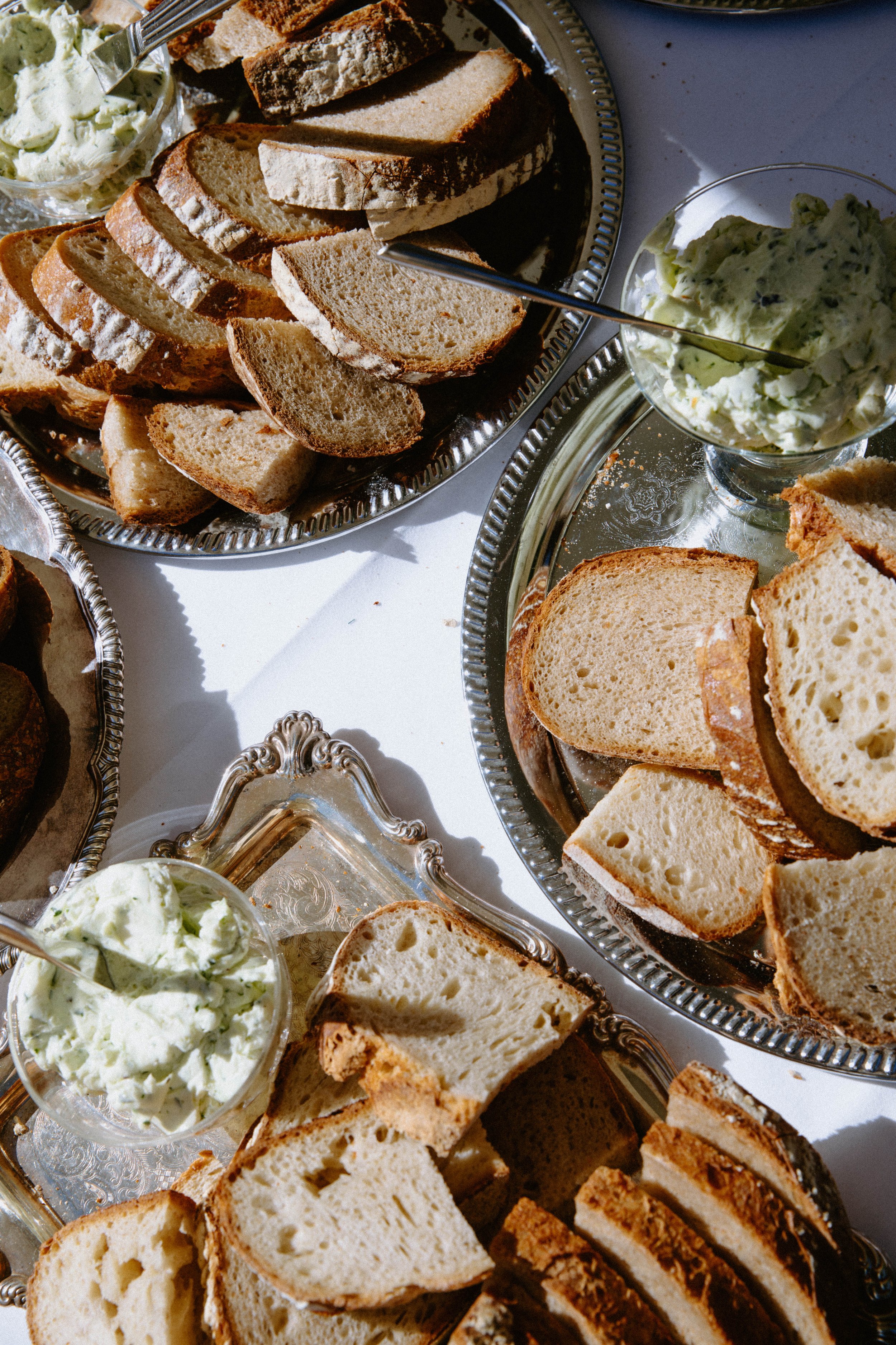 Assorted sliced breads on silver platters, with bowls of herbed butter and cream cheese spread.