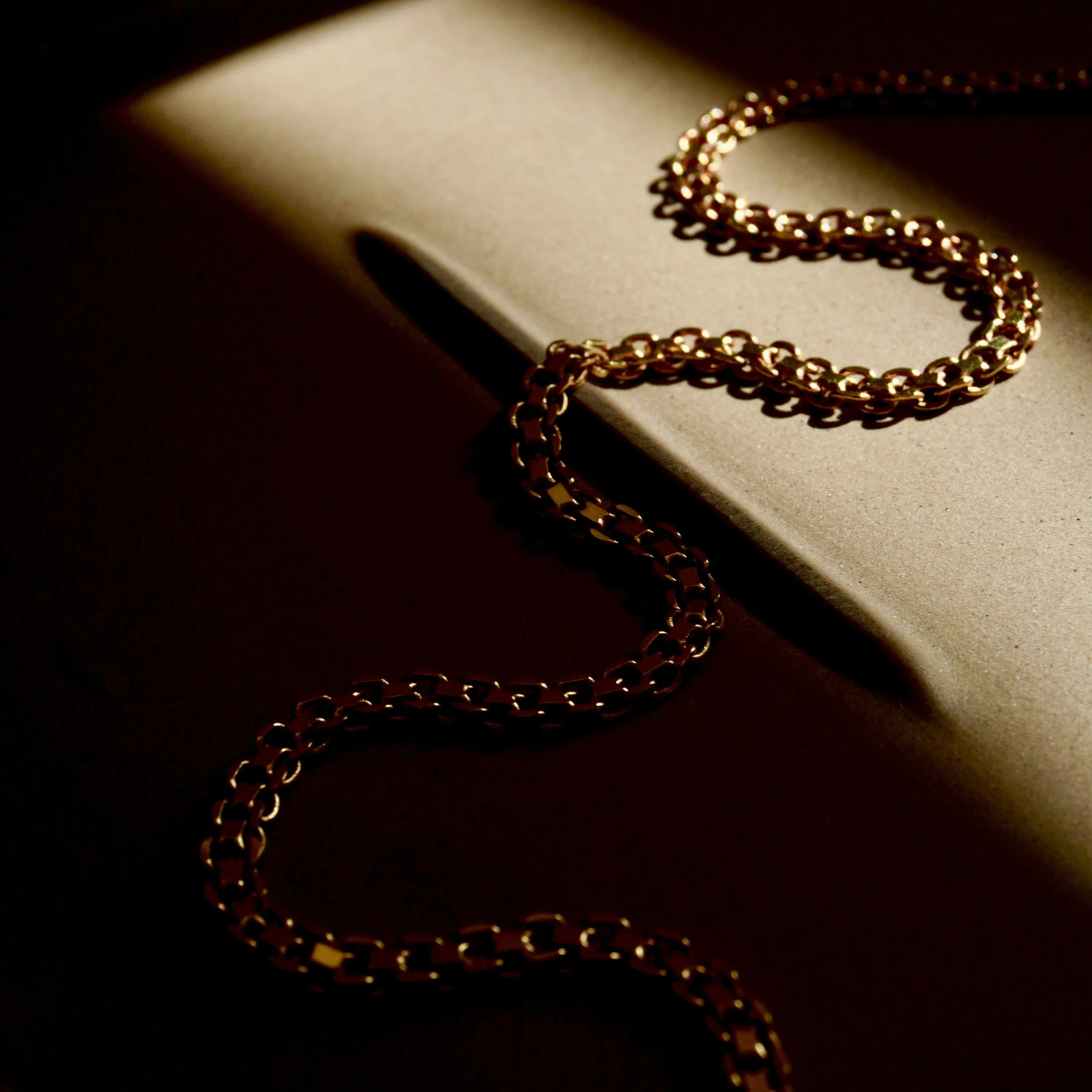 A gold chain necklace draped over the edge of a closed laptop, with a dark fixture creating dramatic shadows.