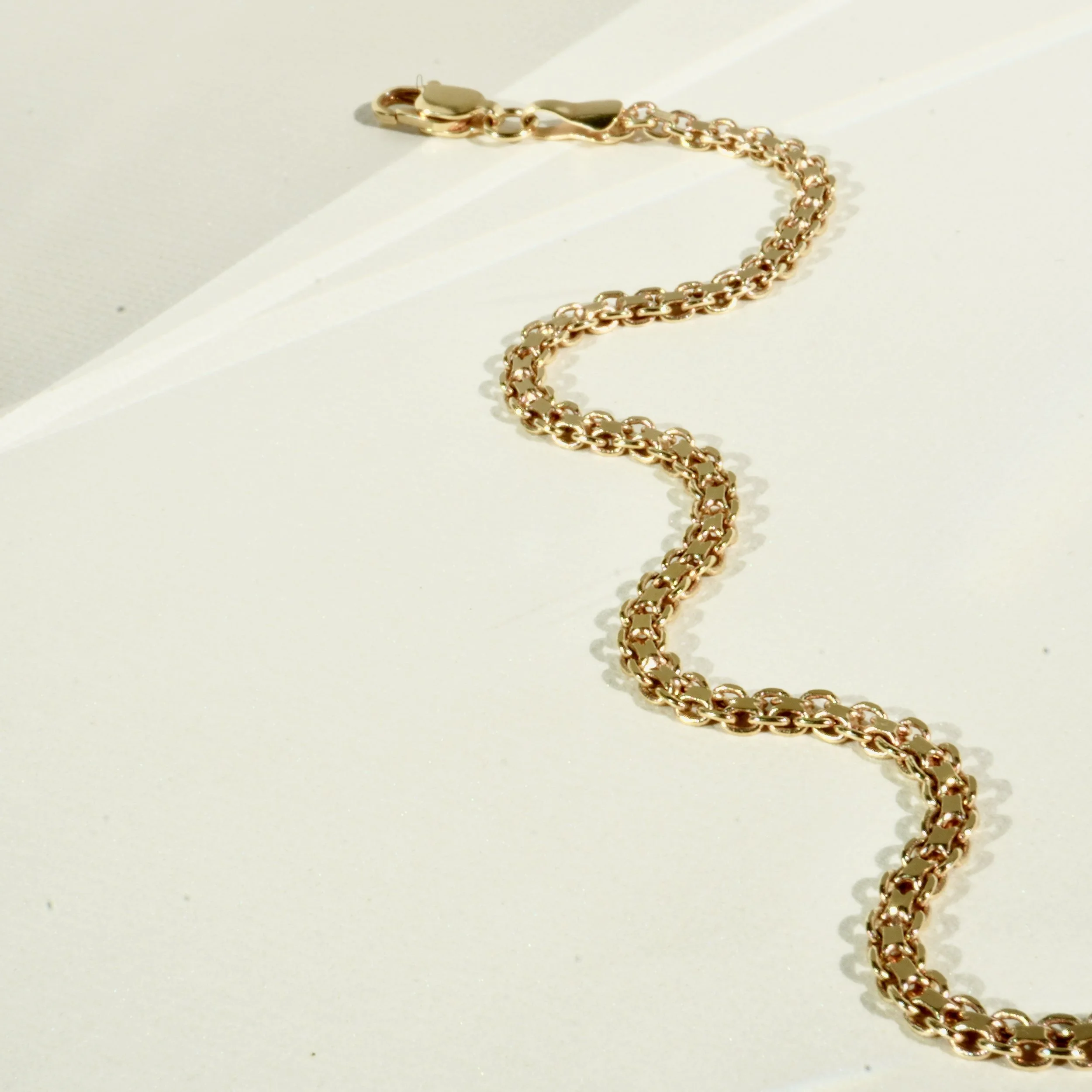 A gold chain bracelet laid out on a white surface with a light-colored background.
