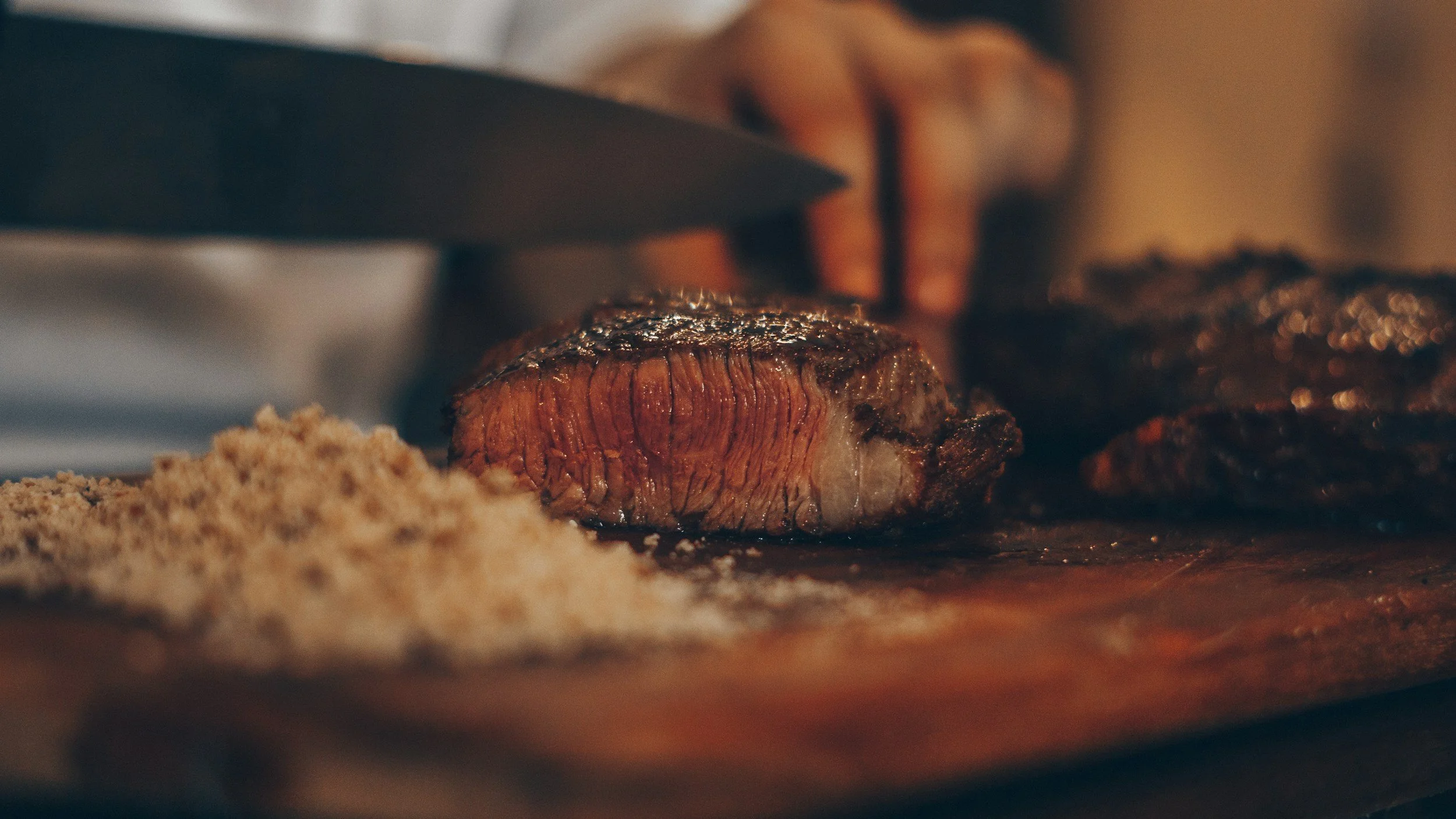 Close-up of a steak being cooked on a grill or pan, with a piece of salt or seasoning nearby.