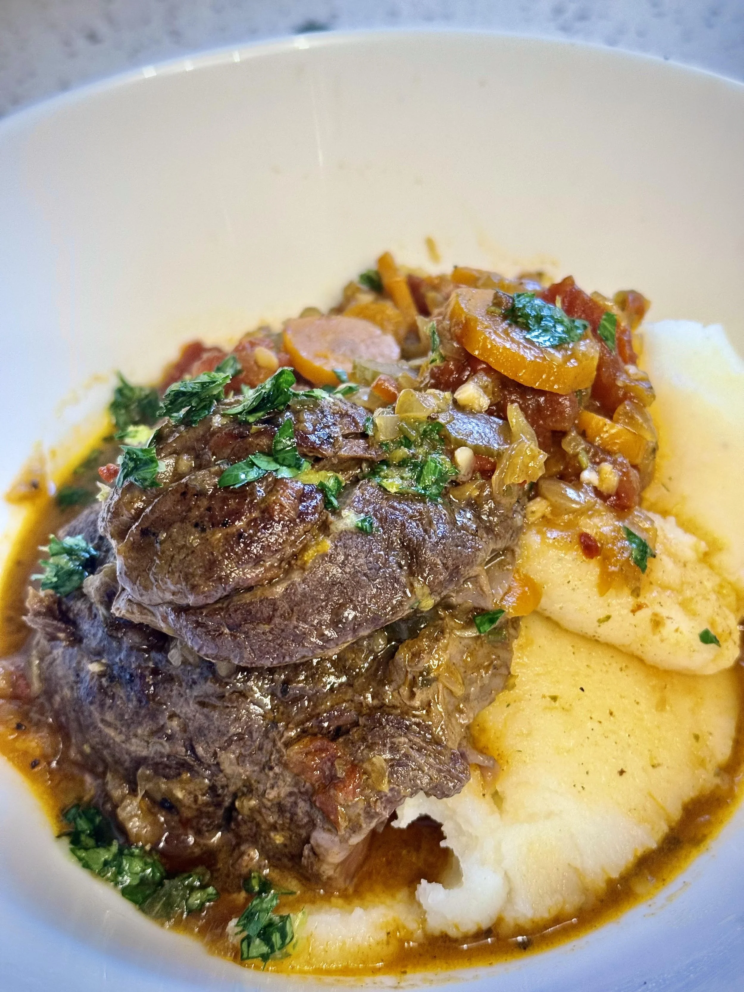 A bowl of beef stew with chopped herbs, served with mashed potatoes.