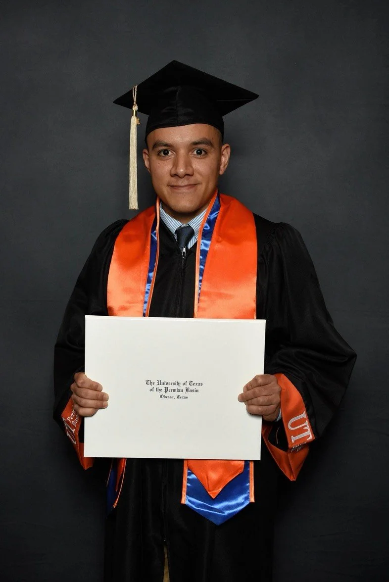 A young man in a graduation cap and gown holding a diploma in front of a dark background.