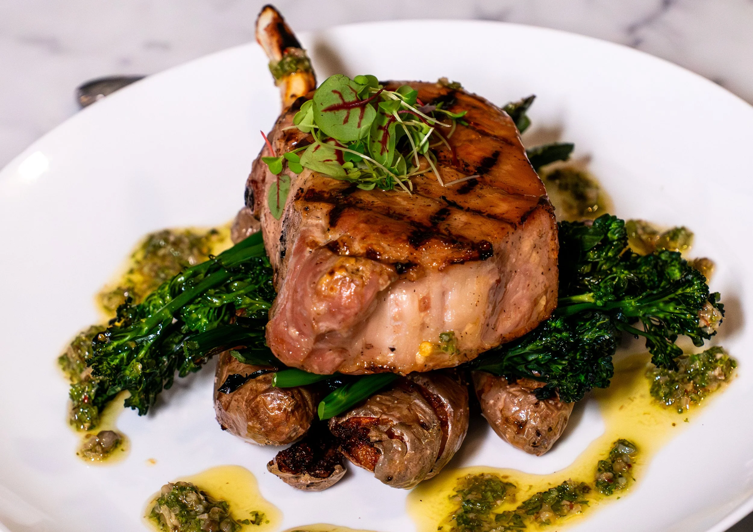 A dish featuring grilled stuffed beef tenderloin topped with microgreens, served with charred broccolini and a herb oil sauce.