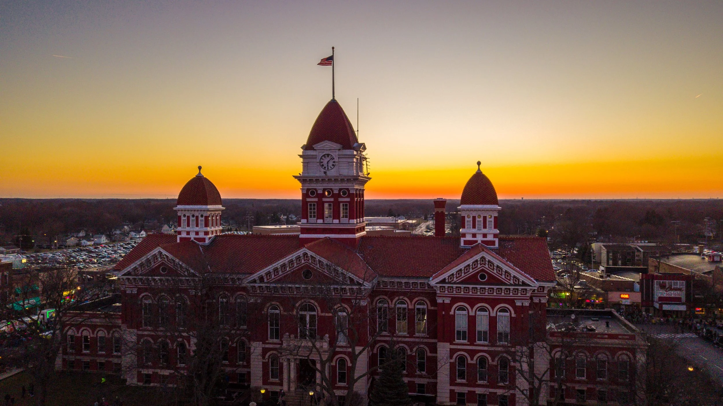 Red brick courthouse with clock tower and flags, sunset sky in the background.