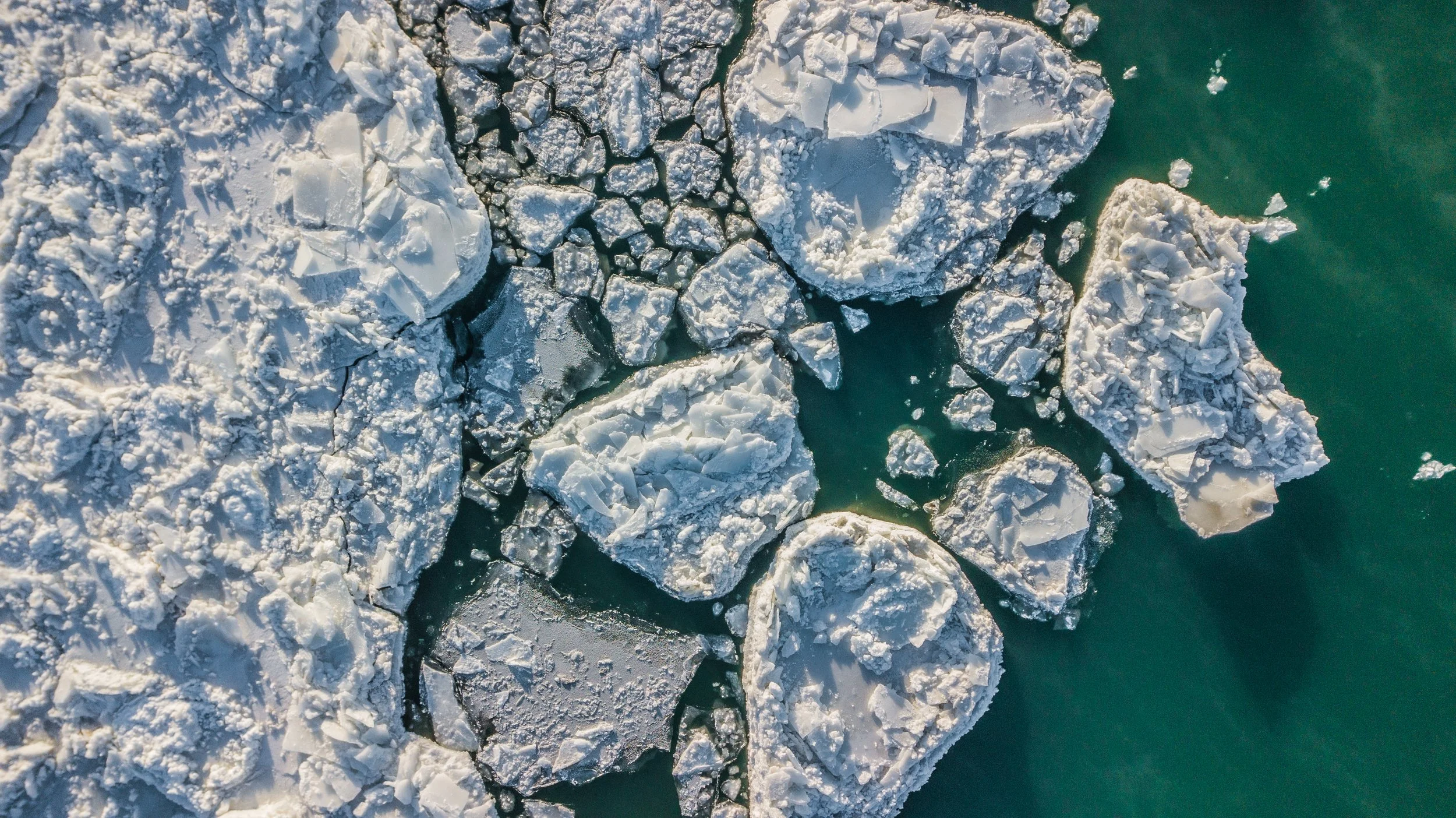 Aerial view of broken ice sheets floating on turquoise water.