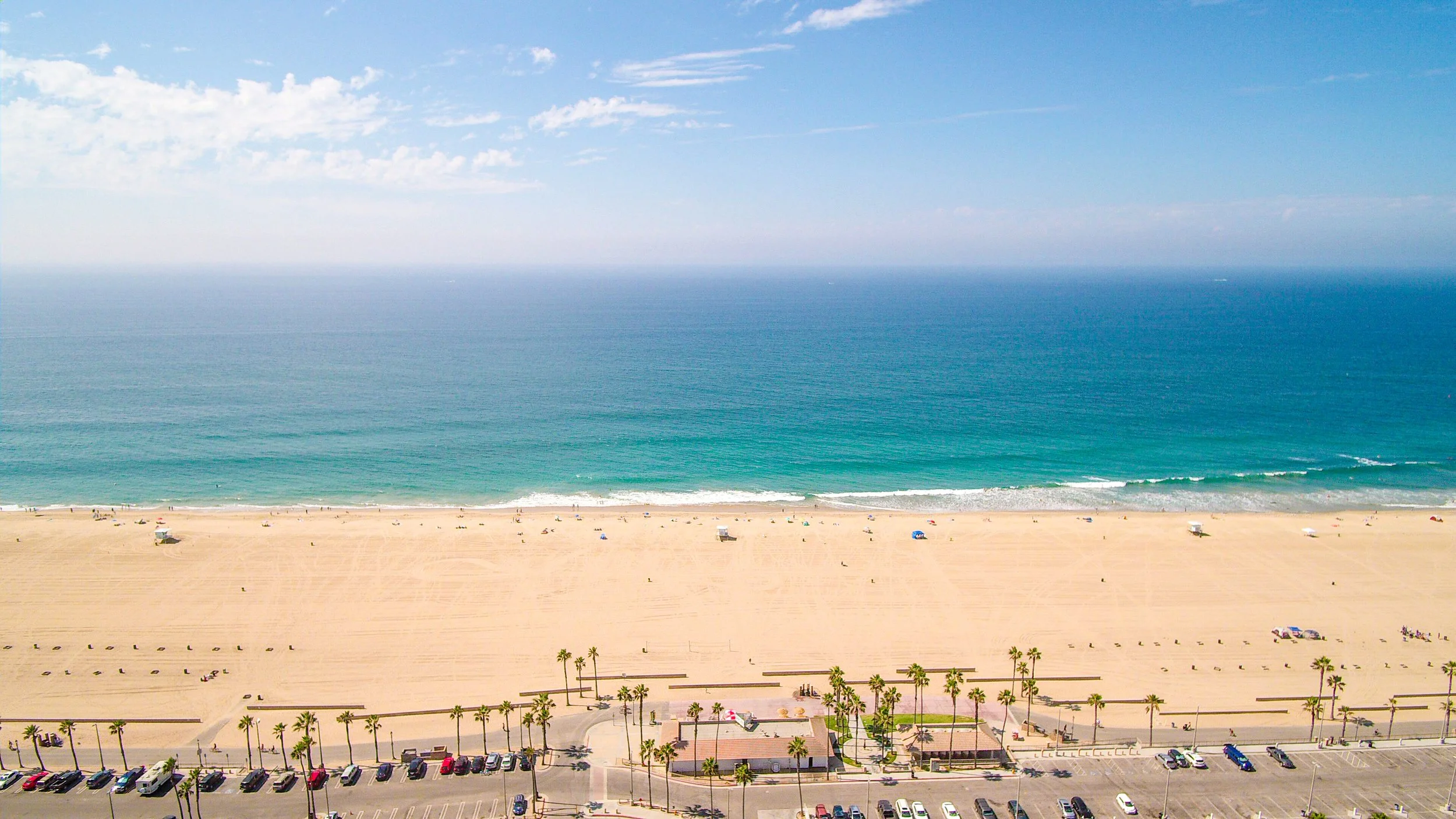 Aerial view of a sandy beach with umbrellas and people, separating the ocean with waves and a clear blue sky.