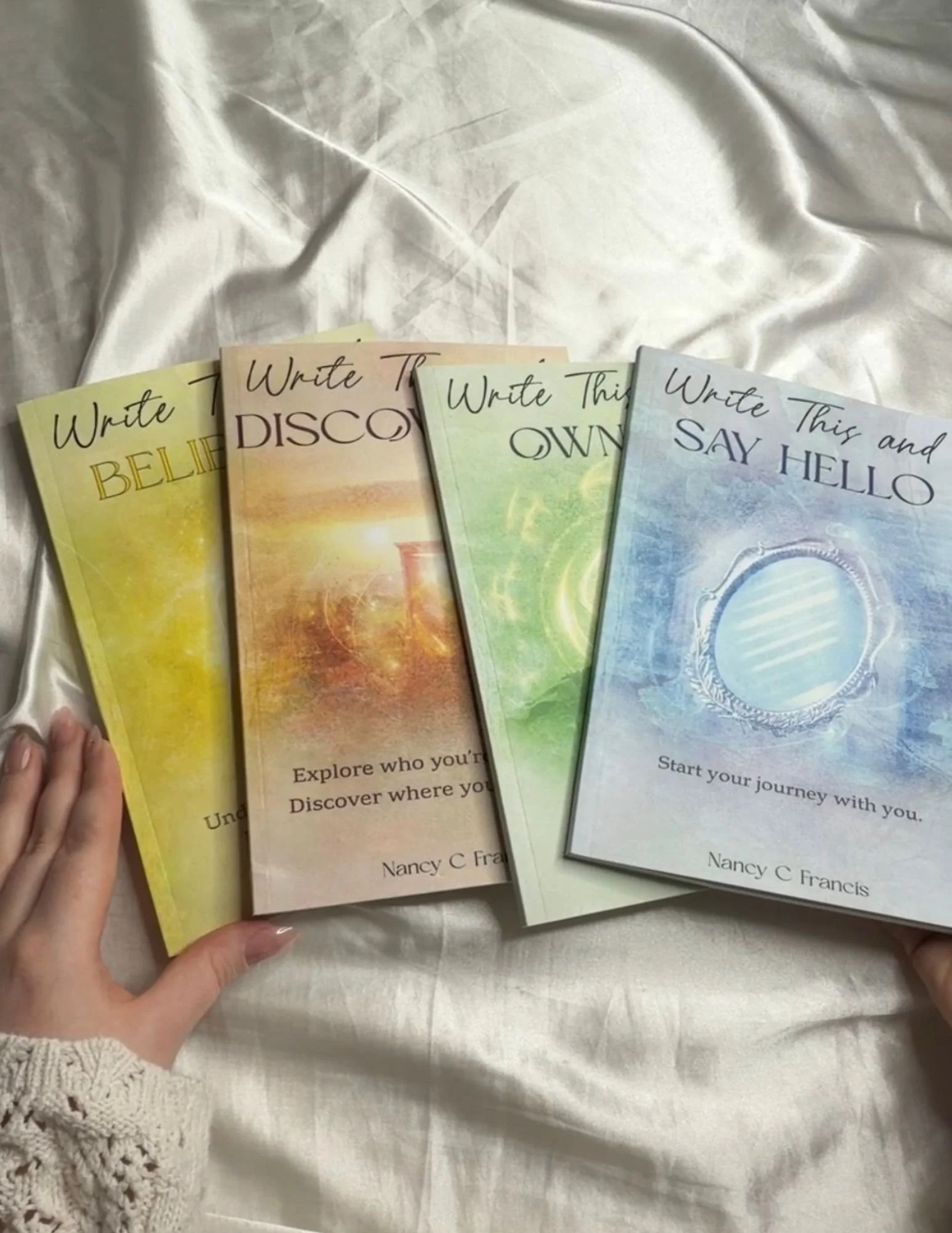 Four guided journals from The Write This Series arranged together on light-colored bedding.