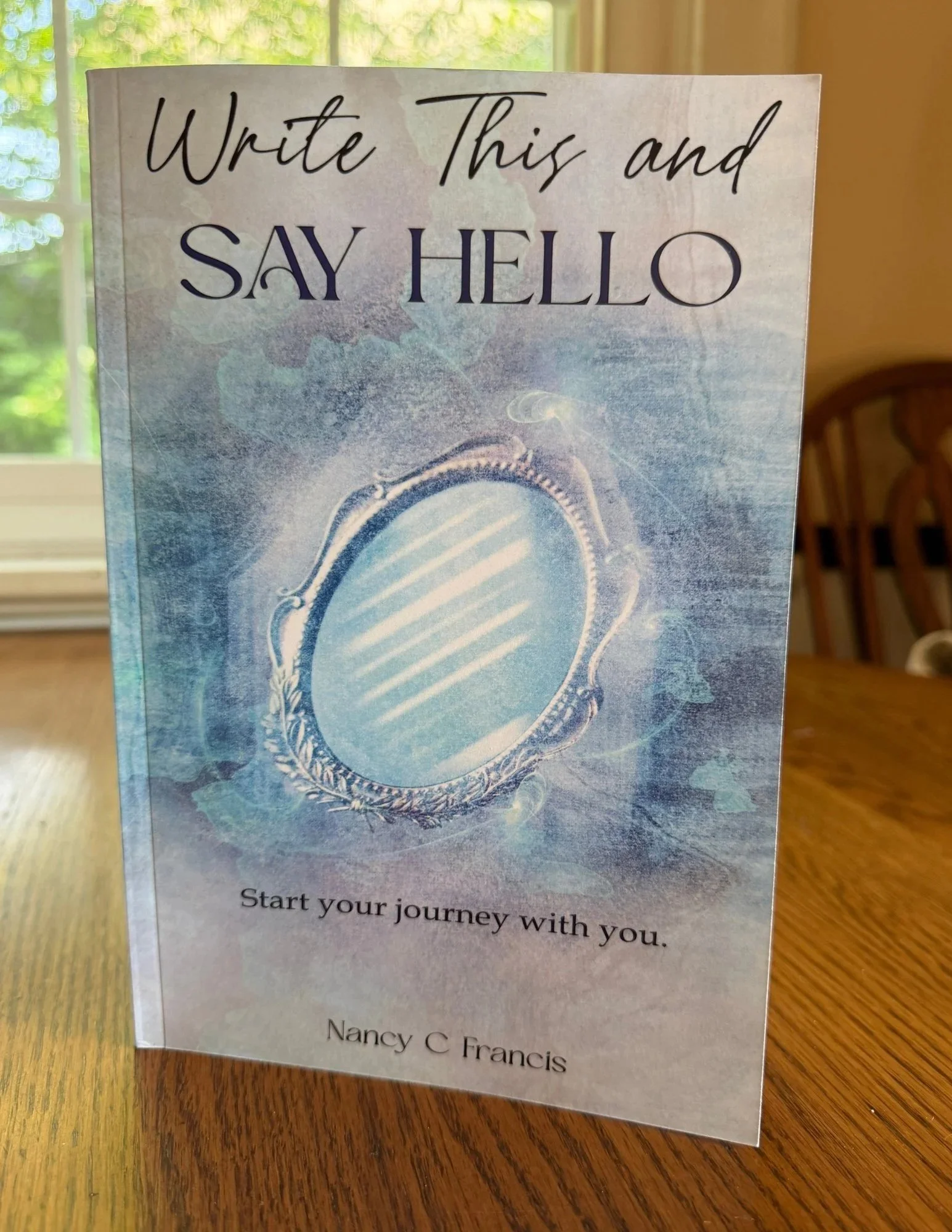 Write This and Say Hello guided journal standing on a wooden table near a sunlit window.