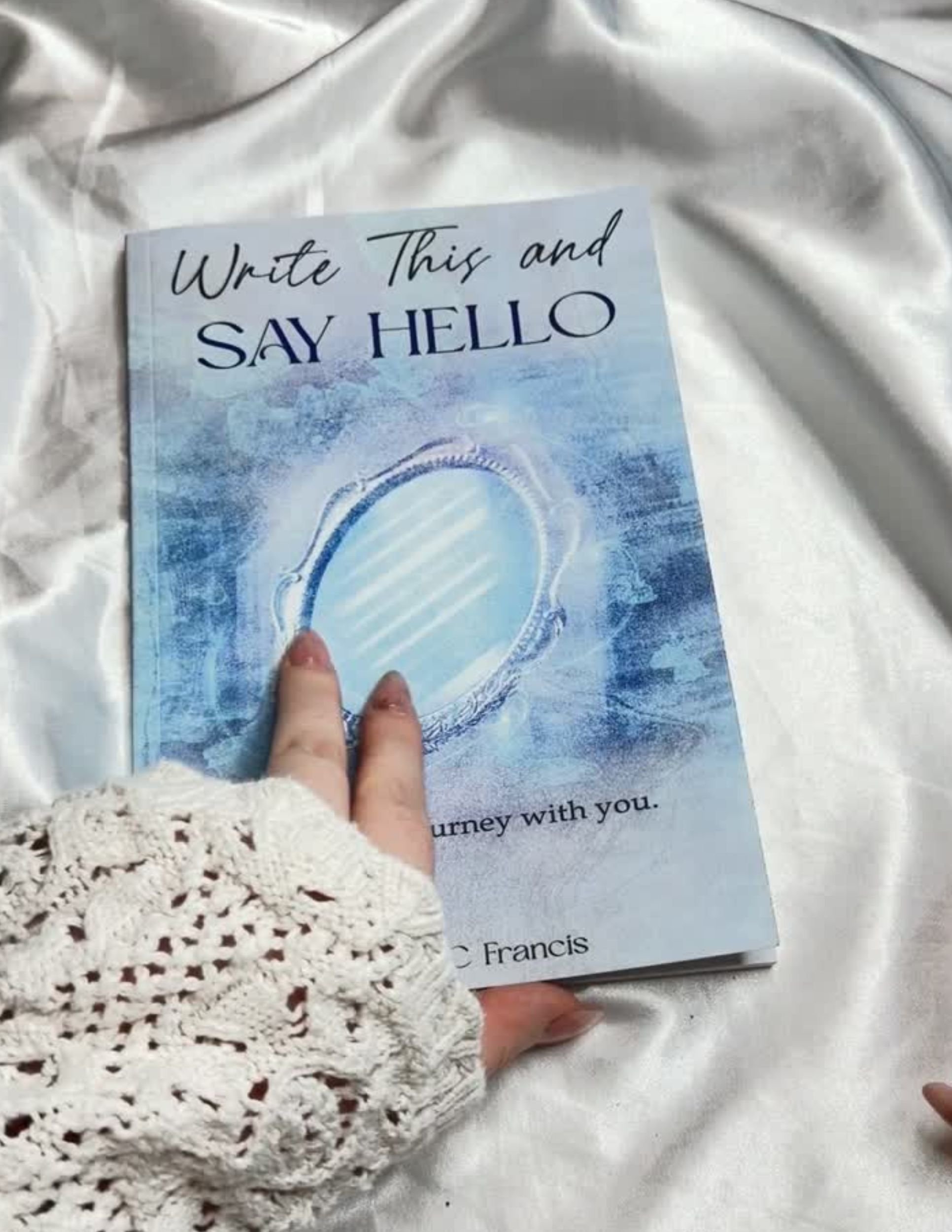 Write This and Say Hello guided journal held against light-colored bedding.