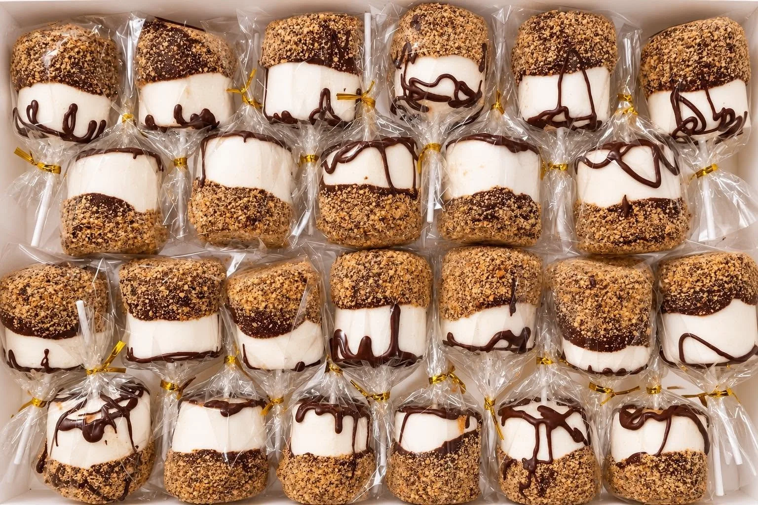Marshmallow pops coated in chocolate and chopped nuts, wrapped in clear plastic, arranged in rows inside a box.