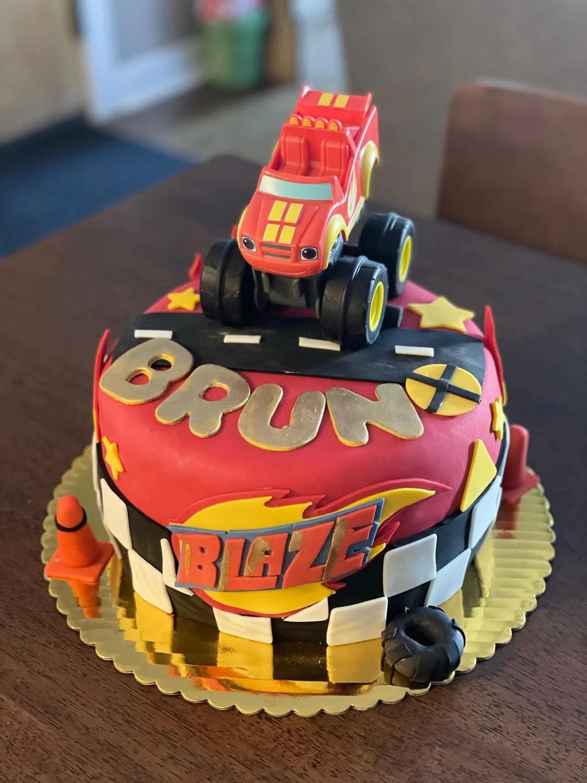 A 3D race car themed birthday cake with race car decorations, the name 'Bruno', and the word 'Blaze' on it, topped with a toy race car.
