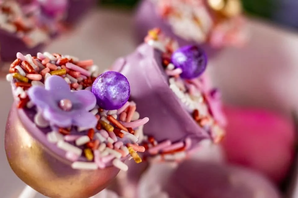 Close-up of decorated cupcakes with purple frosting, colorful sprinkles, and purple candy decorations.