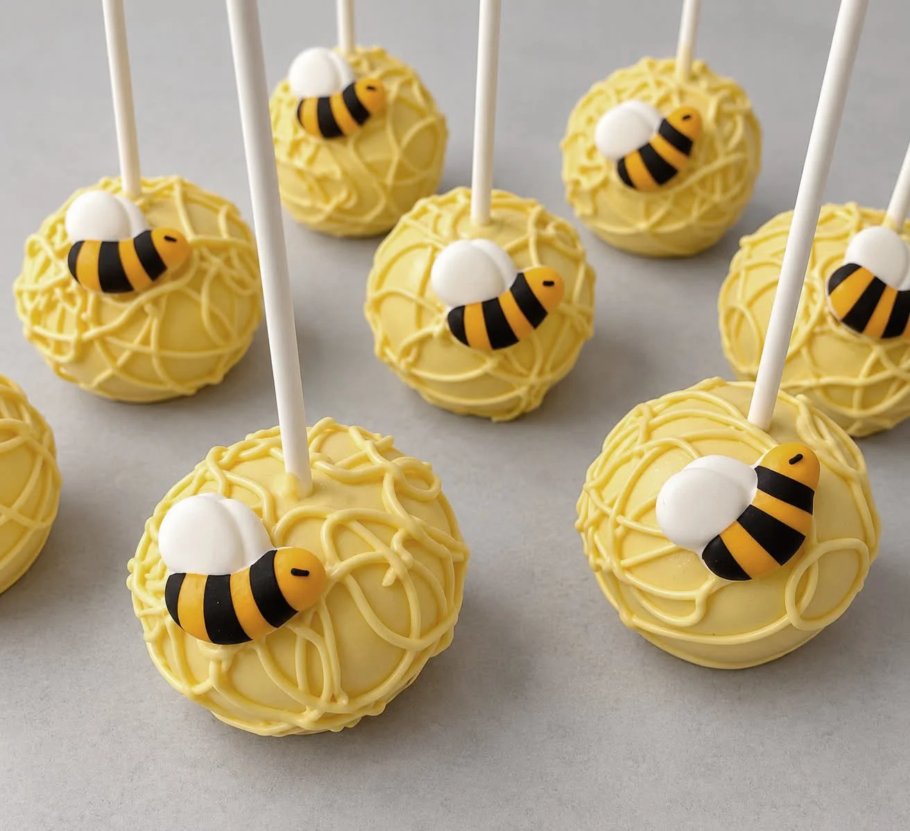 Yellow cake pops decorated with white chocolate drizzle and small bee-shaped toppers.