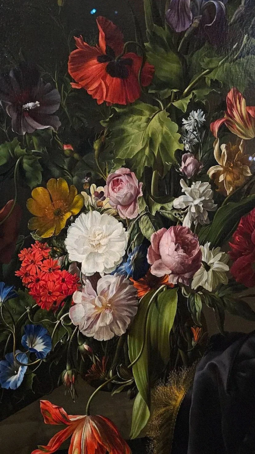 Close-up of a colorful bouquet of flowers including roses, daisies, tulips, and poppies with green leaves against a dark background.