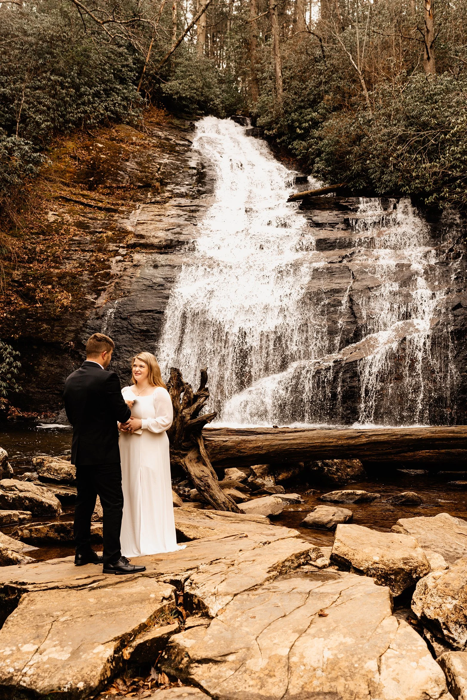 Couple exchanging vow renewal vows on the rocks at the base of Helton Creek Falls surrounded by forest in the North Georgia mountains