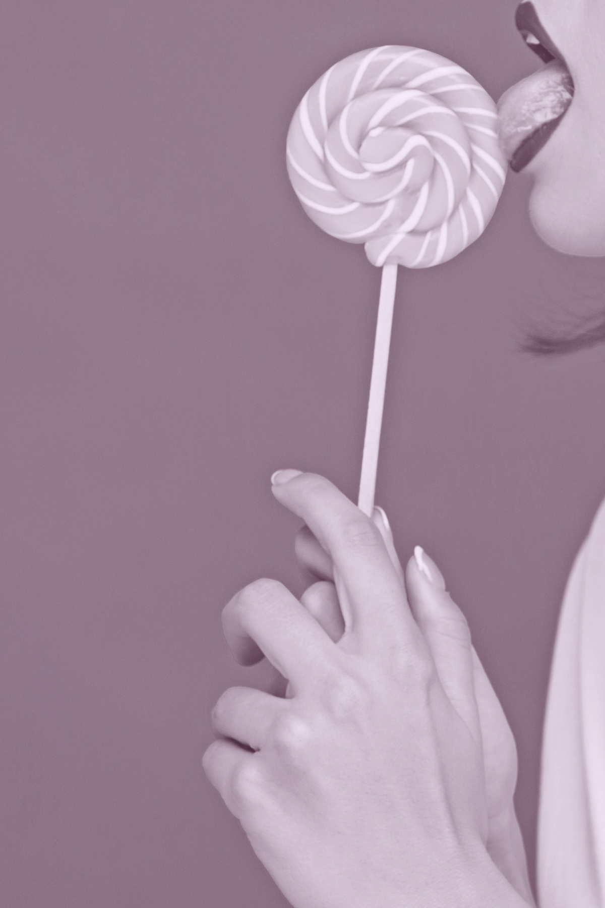 Person holding a large swirl lollipop close to their face, with their tongue sticking out as if about to lick the candy.