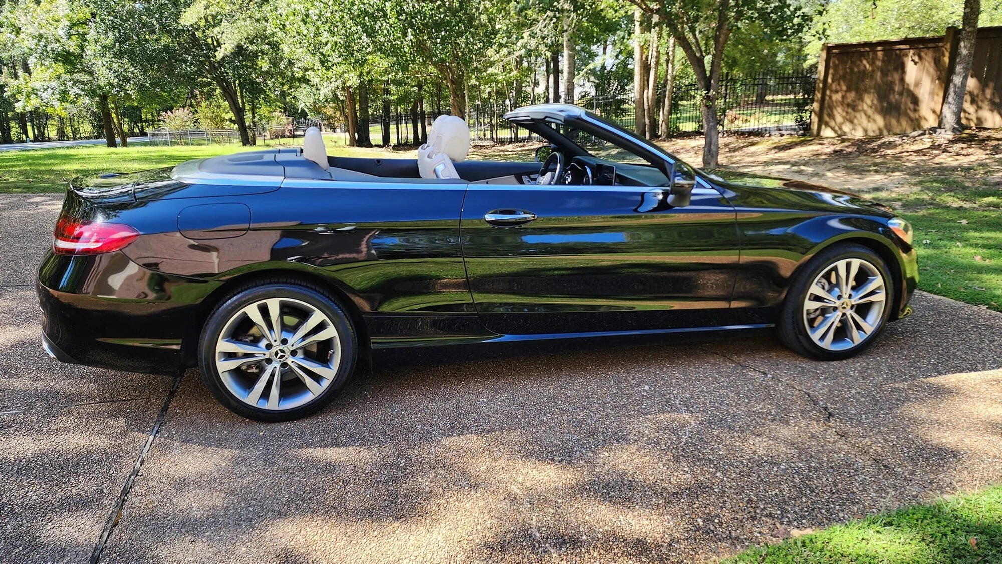 A black convertible car parked on a gravel driveway surrounded by trees and greenery during daytime.