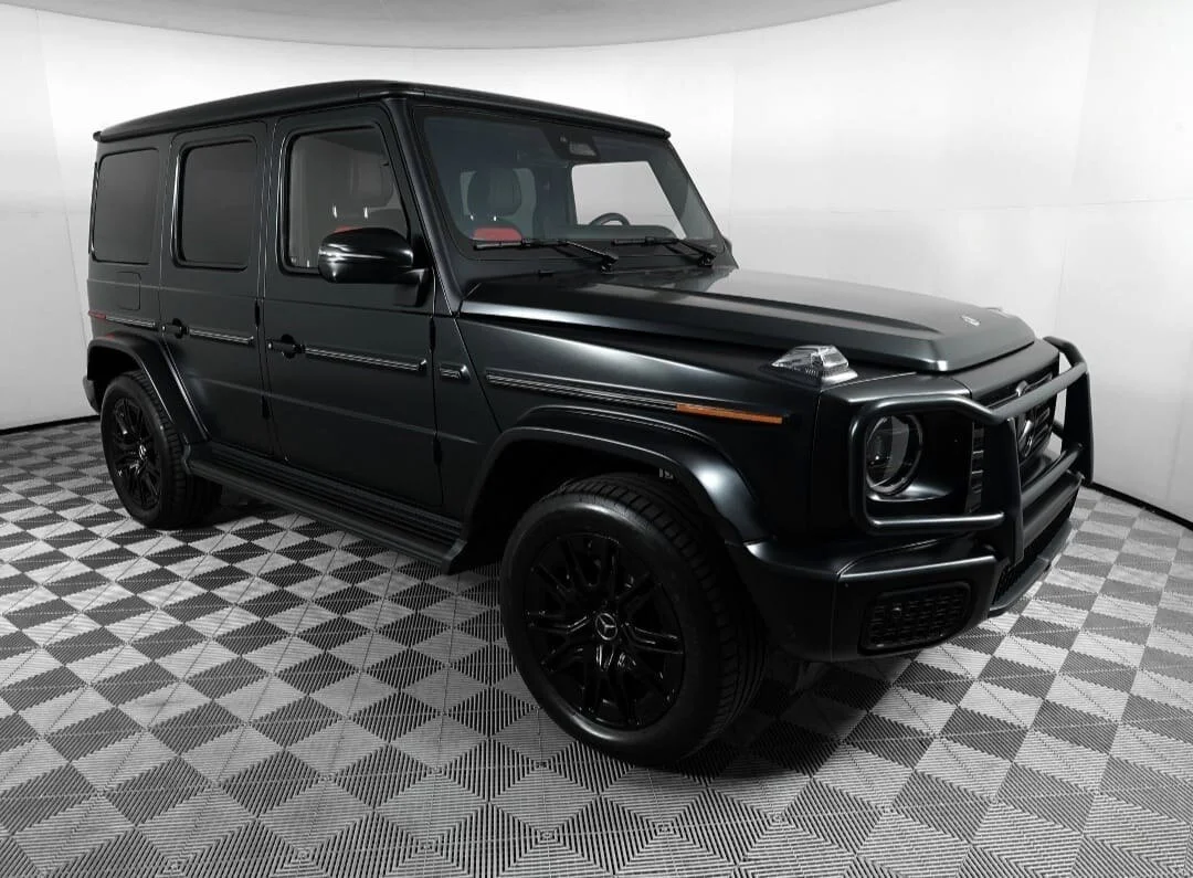 A black Mercedes-Benz G-Class SUV with a custom front grille guard parked in a showroom with a checkered floor.
