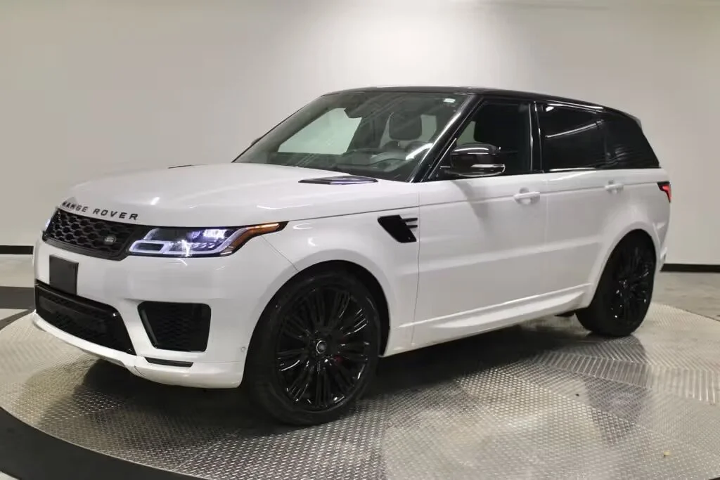 A white Range Rover SUV with black rims, black side mirrors, and a black roof, parked on a metallic platform in an indoor setting.