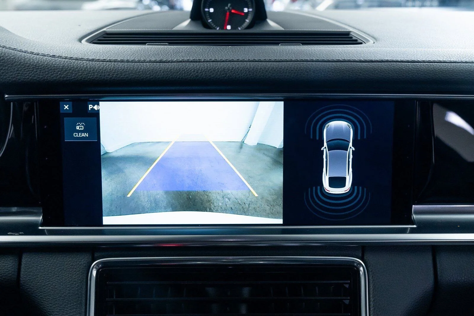 Car's dashboard screen showing a rearview camera feed with parking guidelines and a top-down view of the car indicating proximity sensors
