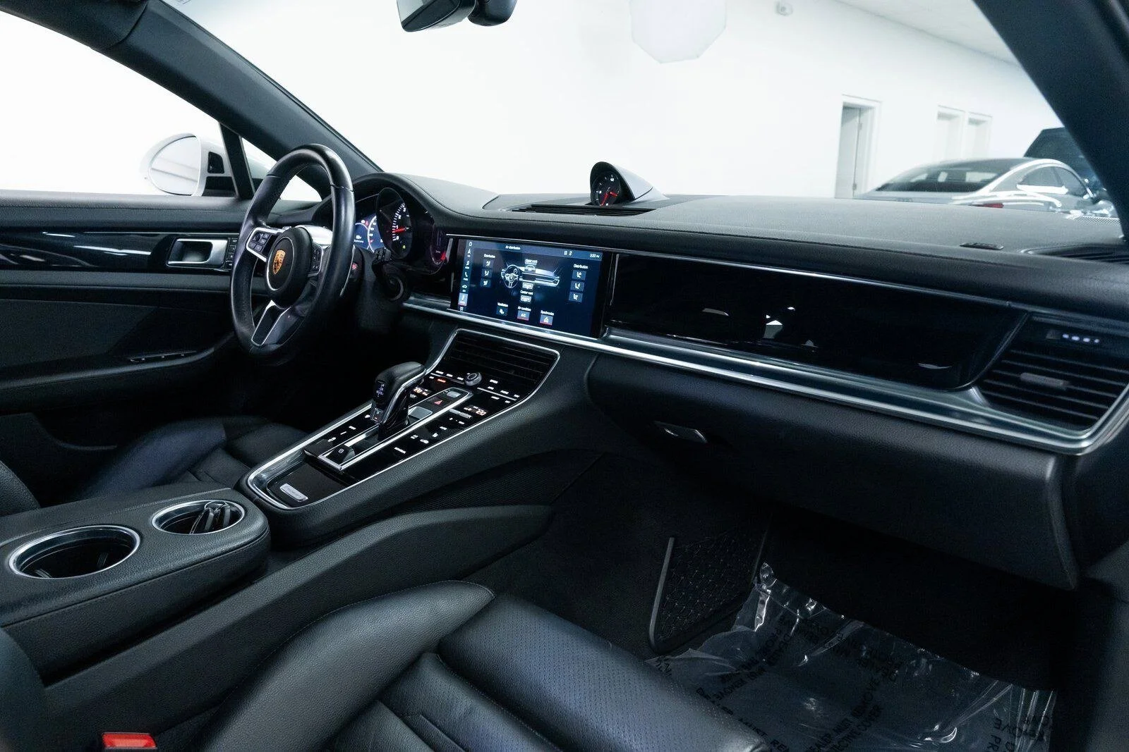 Interior of a luxury car showing the dashboard, steering wheel, touchscreen control panel, gear shift, and cup holders.