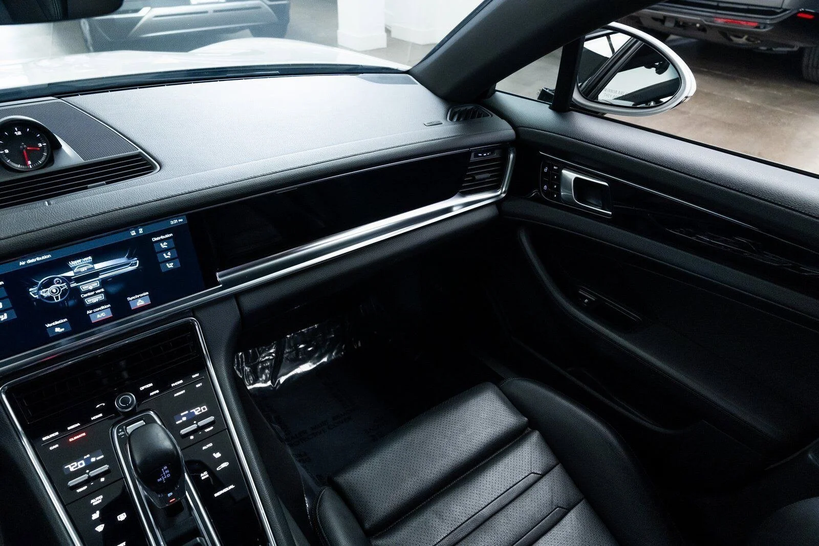 Interior view of a modern car dashboard, showing a digital screen, climate controls, and black leather seat.