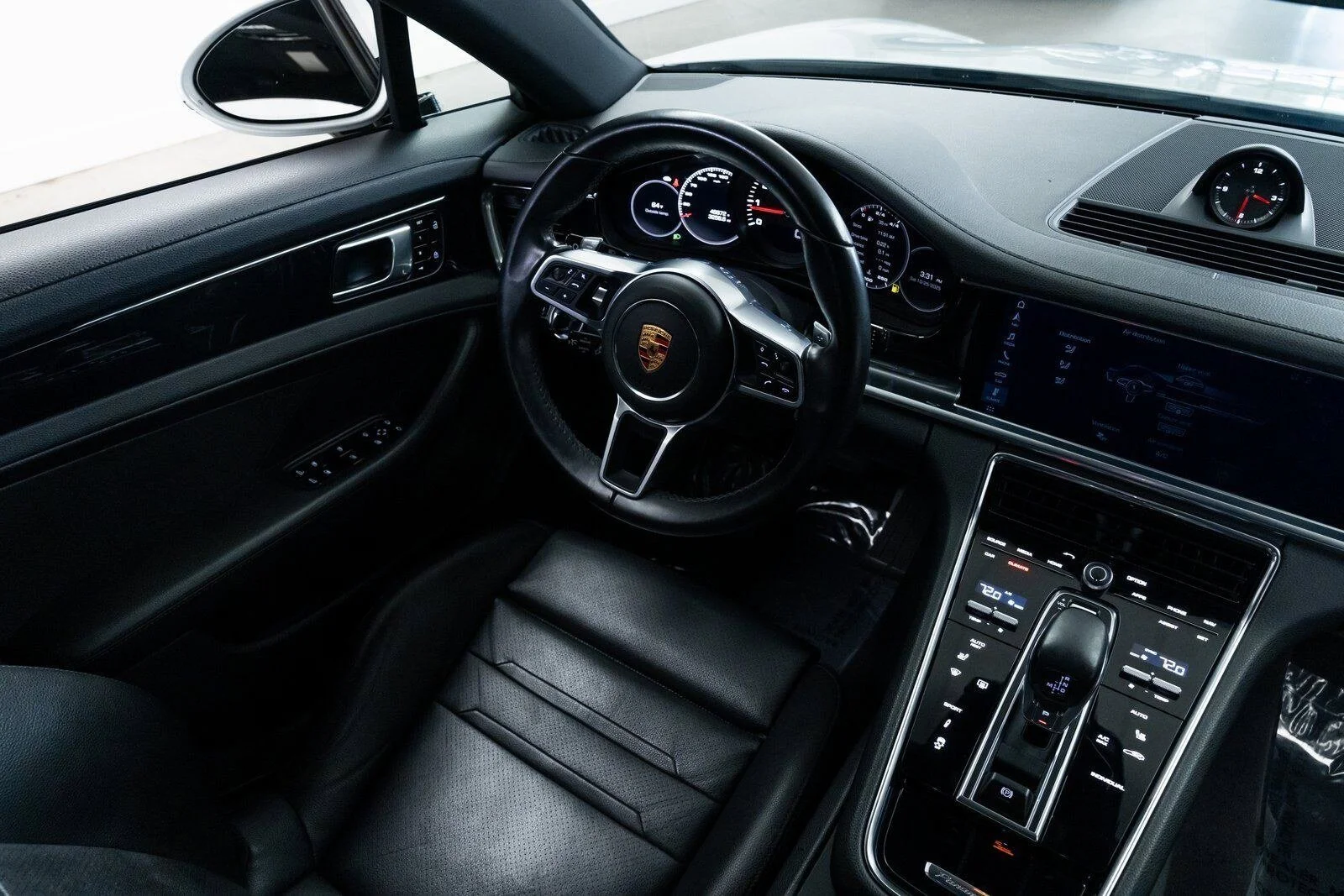 Interior of a luxury car with a black dashboard, steering wheel with Porsche logo, digital instrument cluster, and a center touchscreen display.