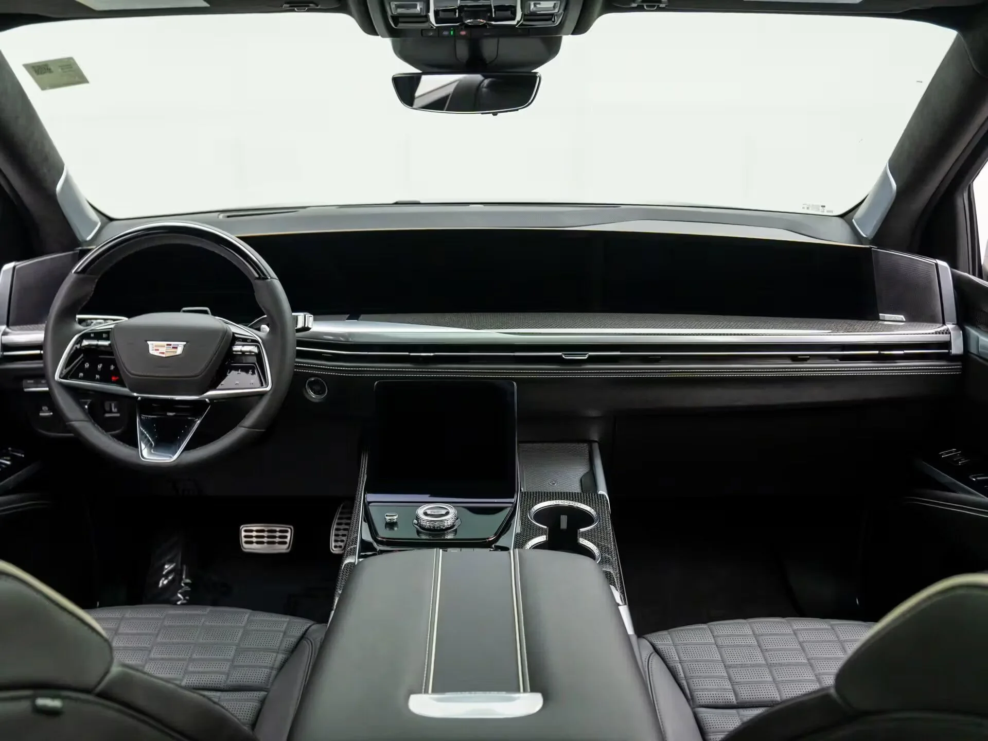 Interior of a modern luxury vehicle, showing the dashboard, steering wheel with Cadillac logo, center console with control knob, digital display, and front seats with quilted upholstery and headrests.