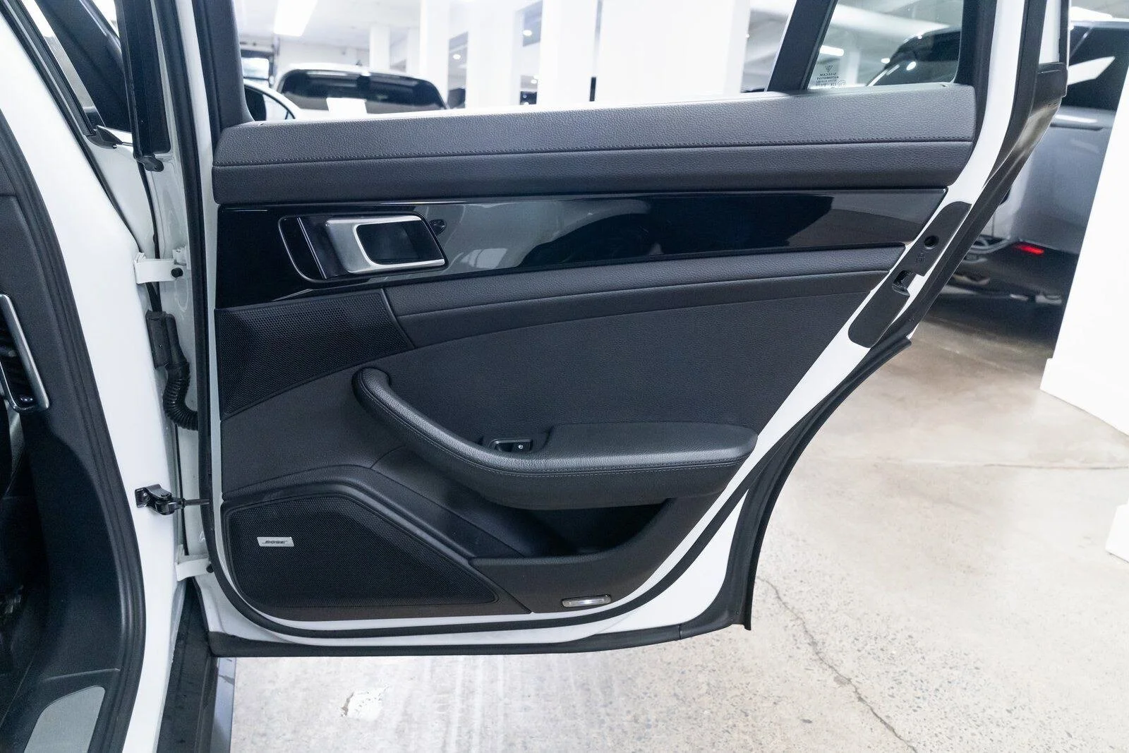 Close-up of a black car interior door panel with a silver handle, speaker, window control, and armrest in a showroom.