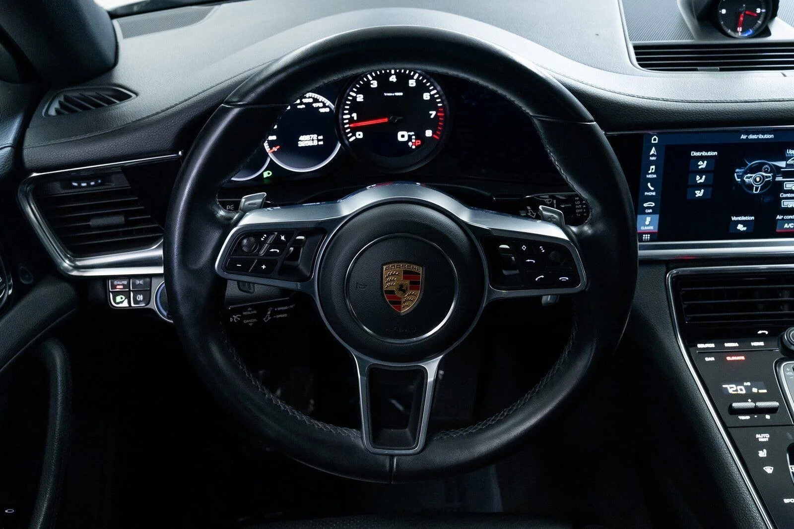 Dashboard view of a Porsche car interior, featuring steering wheel with Porsche emblem, digital and analog gauges, and a digital touchscreen display showing climate controls and air distribution.