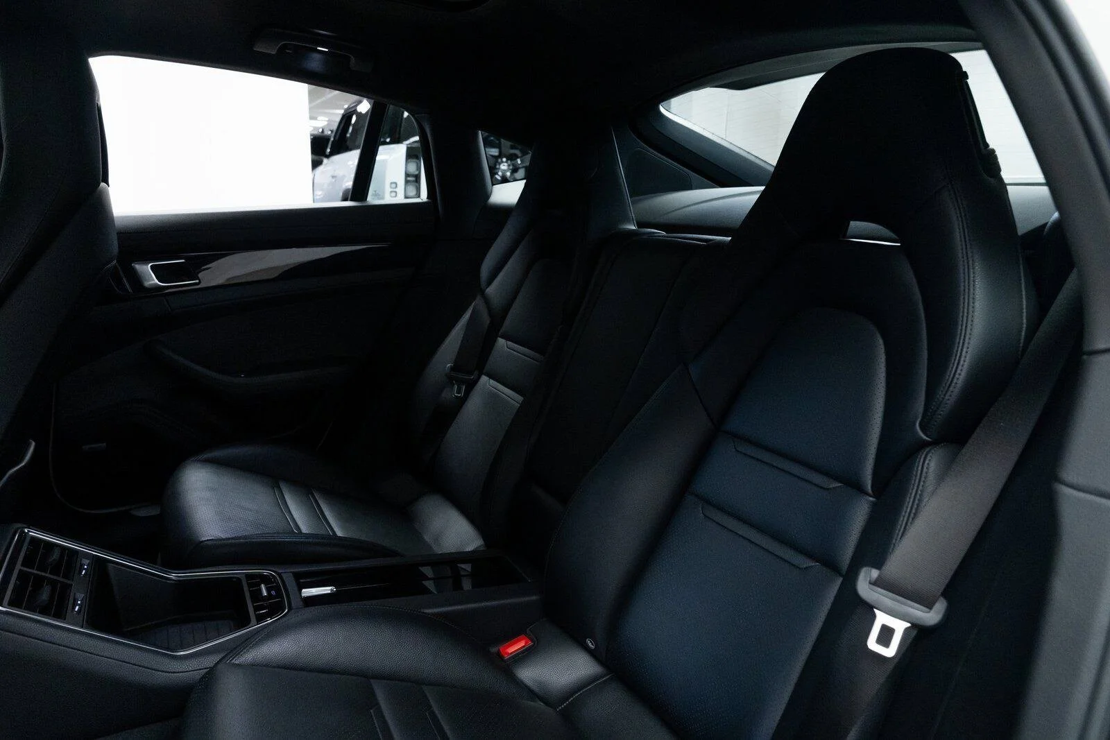 The interior of a modern luxury car's backseat area with black leather seats, seat belts, and a central console.