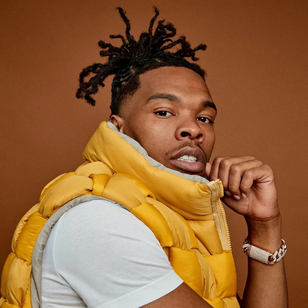 Portrait of a young man in a yellow puffer vest and white t-shirt, looking at the camera against a brown background.
