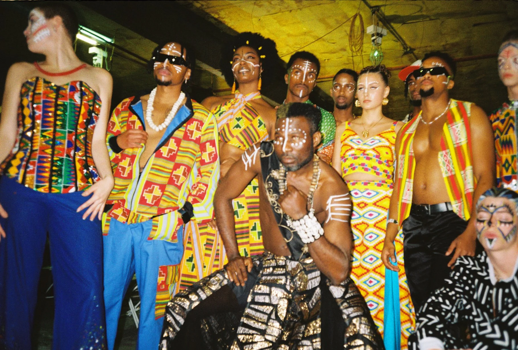 Group of people dressed in traditional African attire with face paint and accessories, standing together indoors.