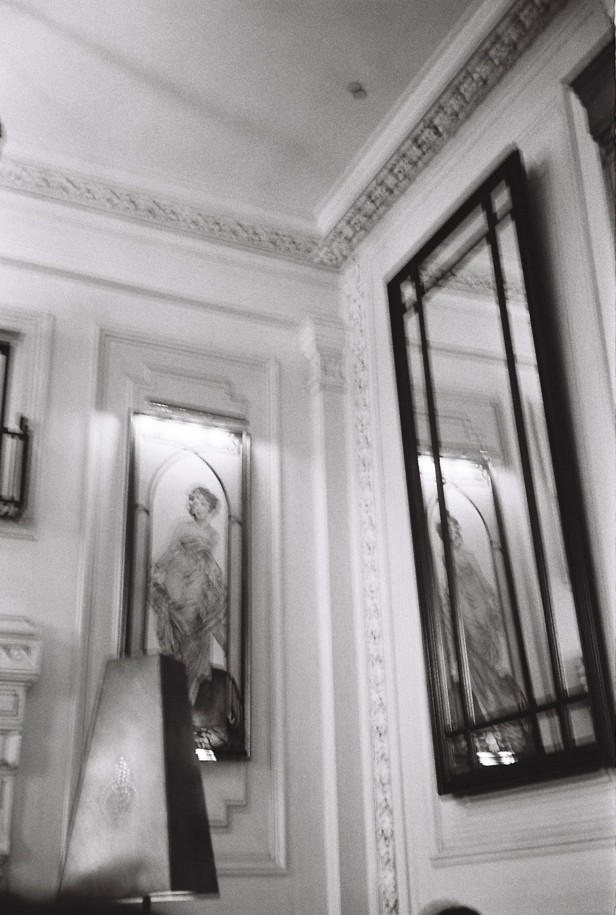Interior of an ornately decorated room with detailed molding on the walls and ceiling, featuring black-and-white portraits of women in ornate frames.