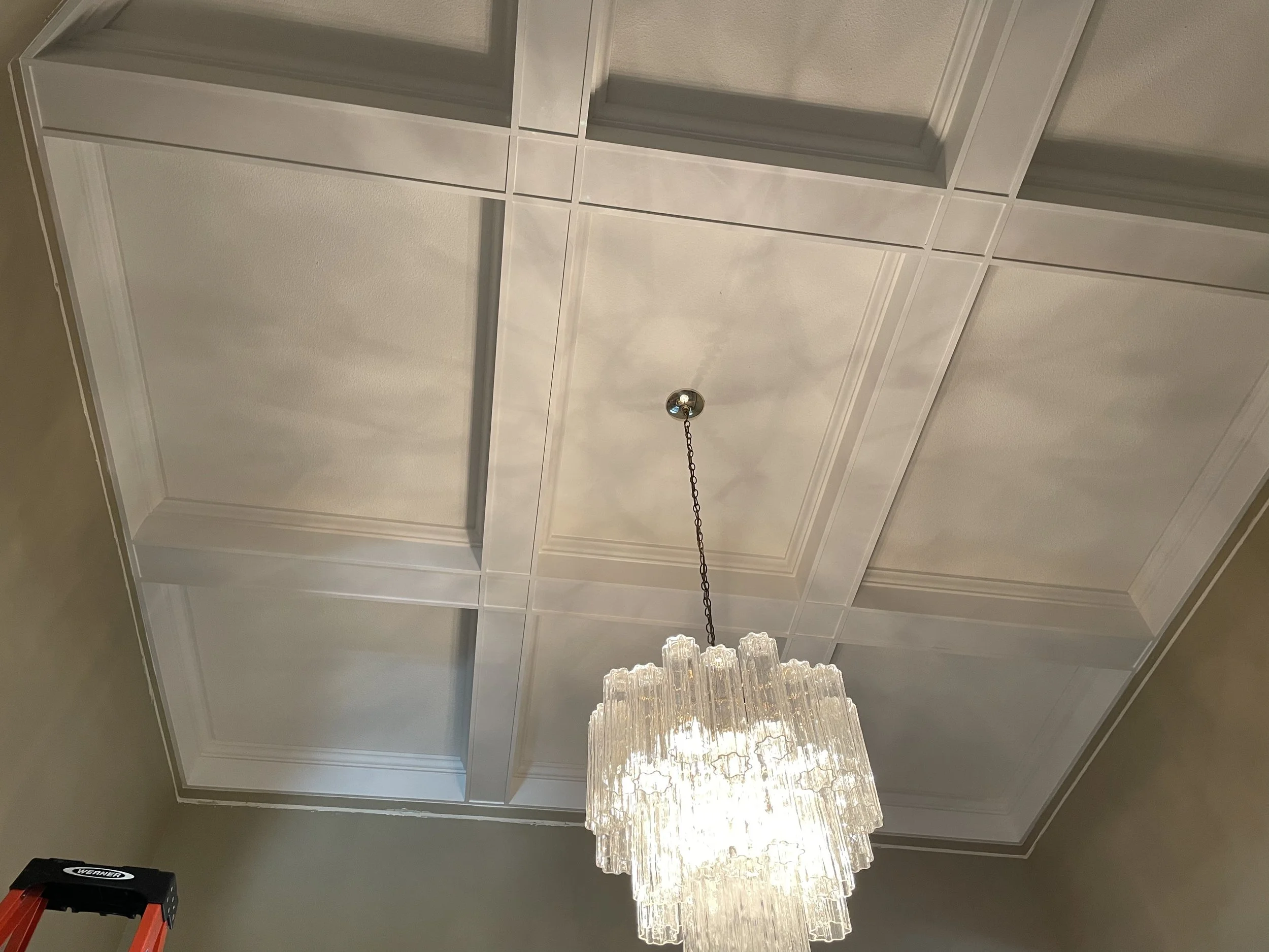 Ceiling with a chandelier and decorative molding on white walls.