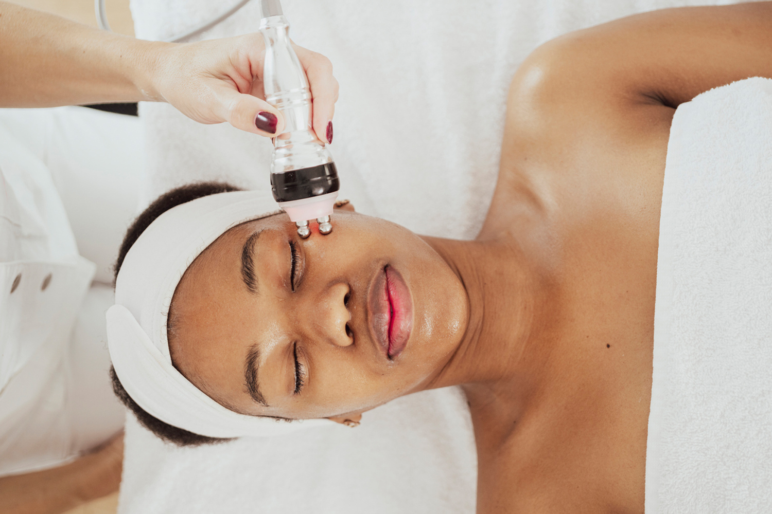 Relaxed woman receives a professional facial treatment with a handheld skincare device.
