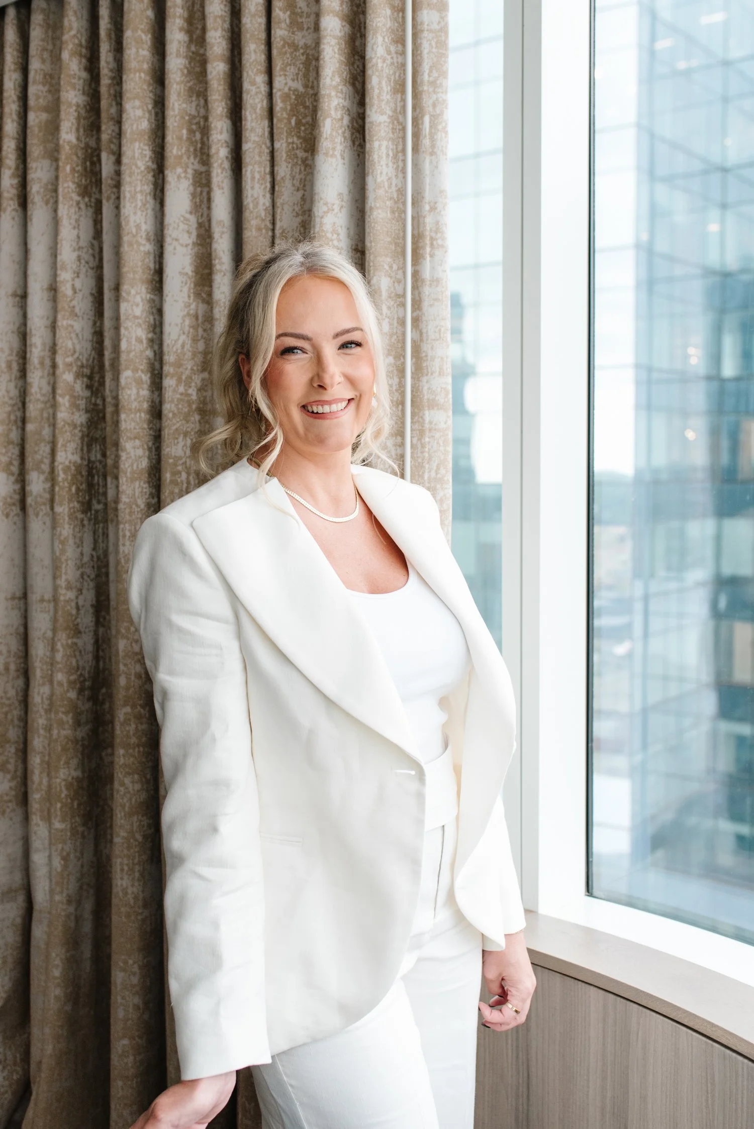 Keynote speaker Jenna Shaw smiling in a white suit beside a high-rise window