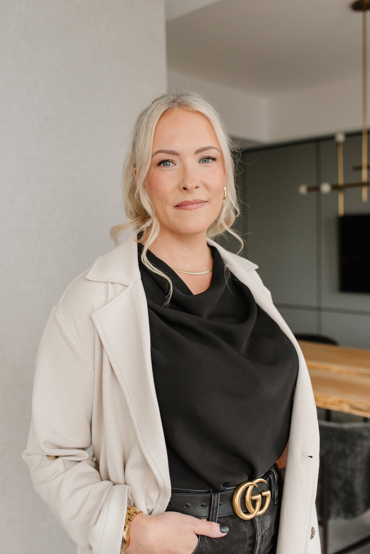 Jenna Shaw standing in a modern dining room wearing a beige trench coat and black blouse