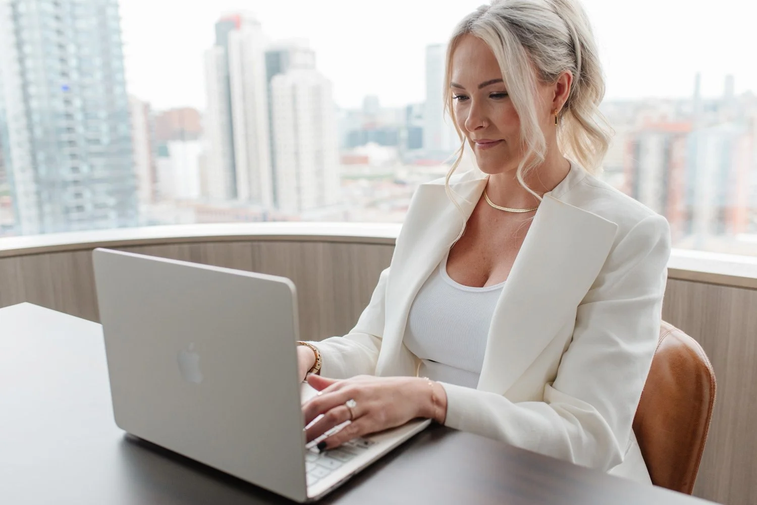 Jenna Shaw typing on a laptop at a desk with a downtown skyline behind her