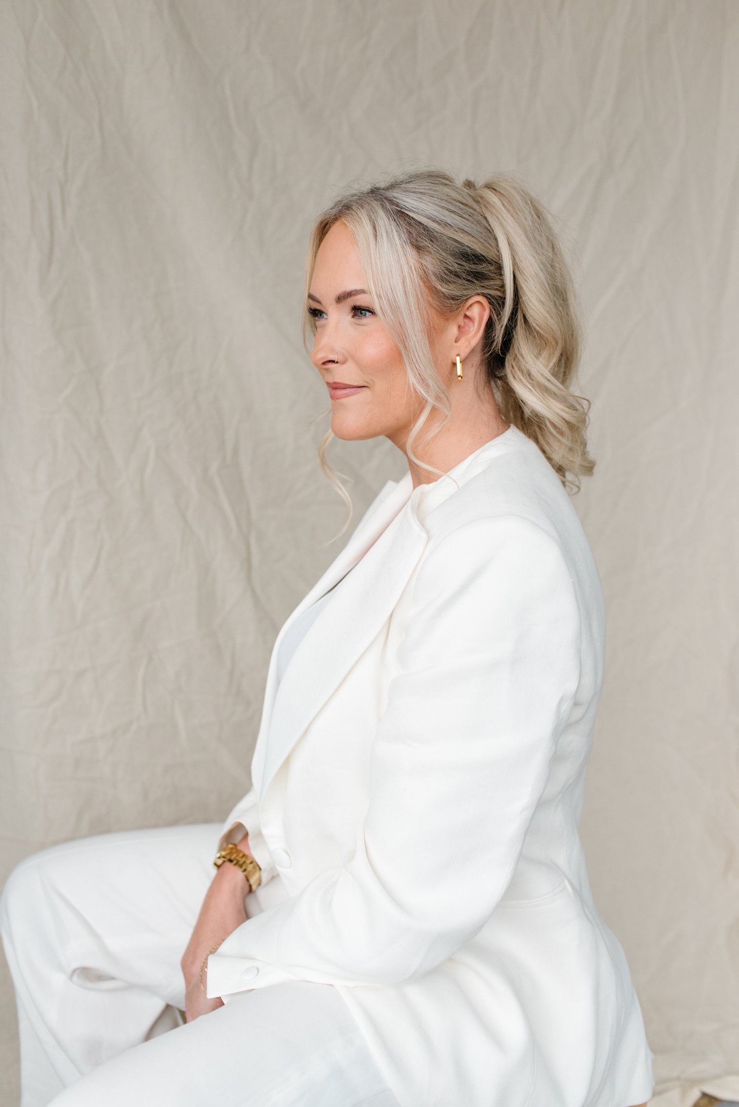 Side profile of Jenna Shaw seated in a white suit, smiling softly against a linen backdrop
