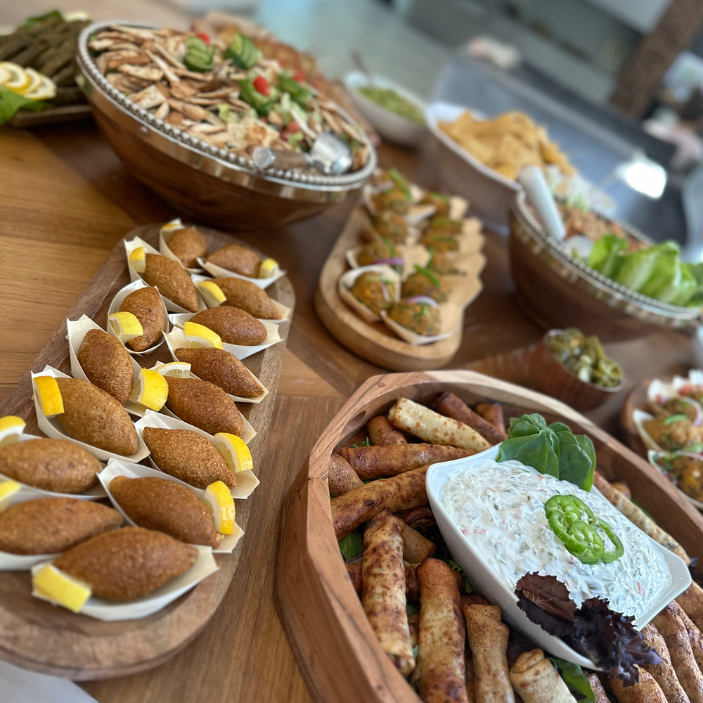 Assorted dishes including fried foods, salads, dips, and appetizers on a wooden table, likely for a gathering or party.