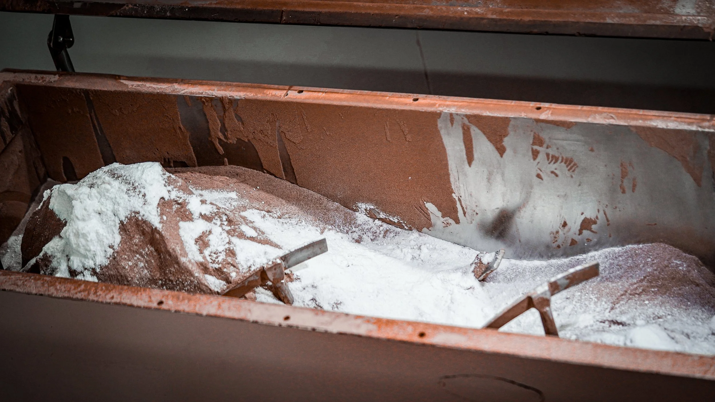 Close-up of a rusty metal surface with white powdery debris, possibly chalk or plaster, scattered on the surface.