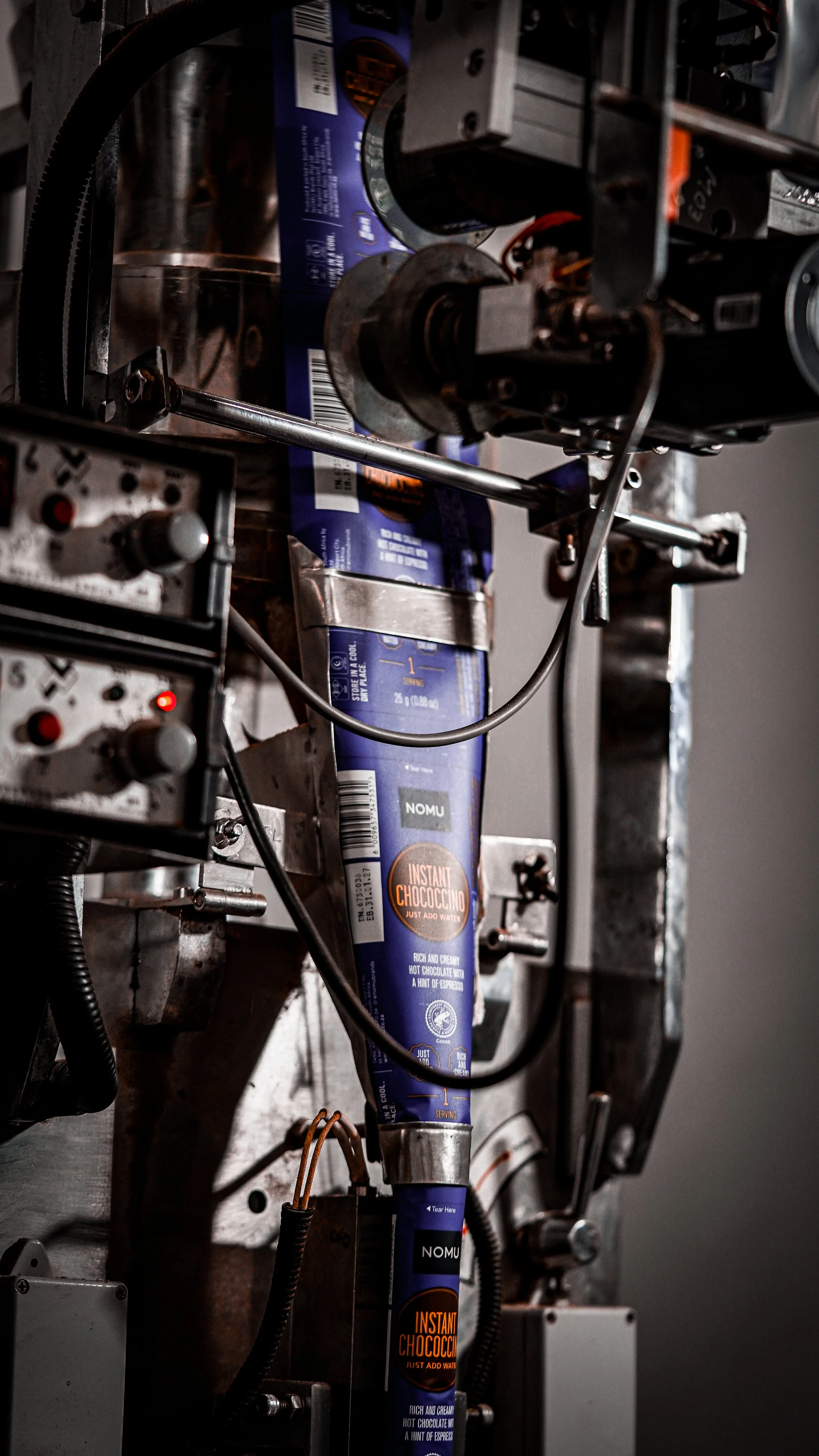 Industrial machinery with a large, blue cylindrical container labeled "Instant Chococino." The machine has various metal parts, pipes, and wires.