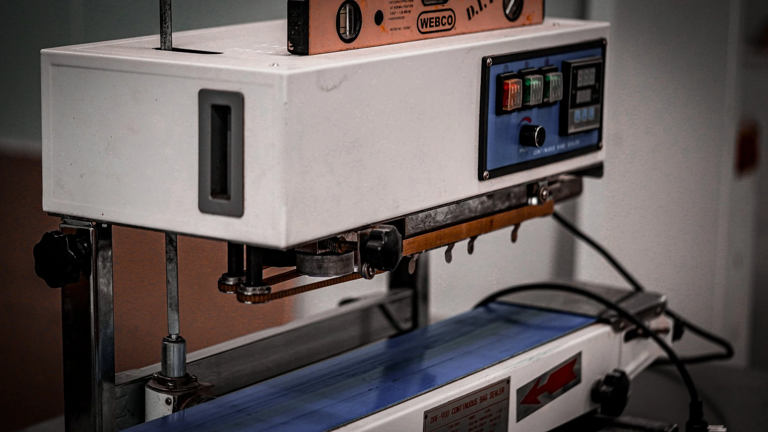Medical device with digital controls, buttons, and a dial, connected to a conveyor belt system with a blue surface.