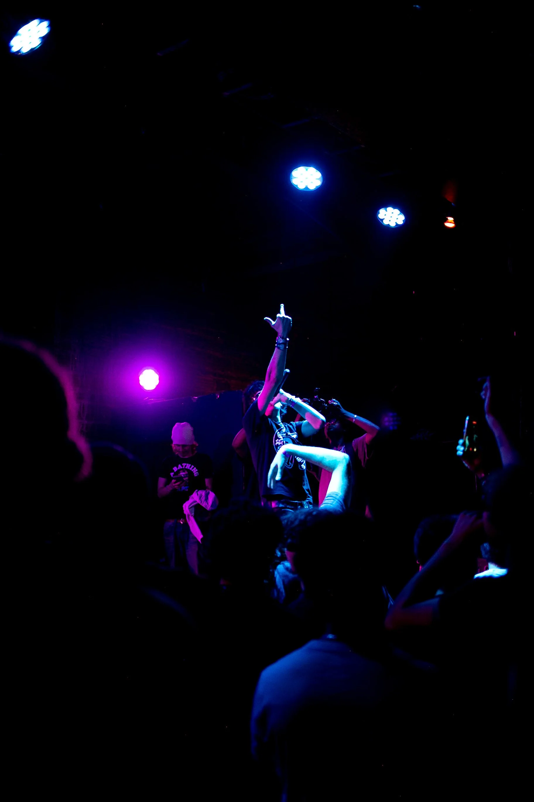 People dancing and enjoying live music on a dark stage with colorful lights, including purple and blue, illuminating the scene.